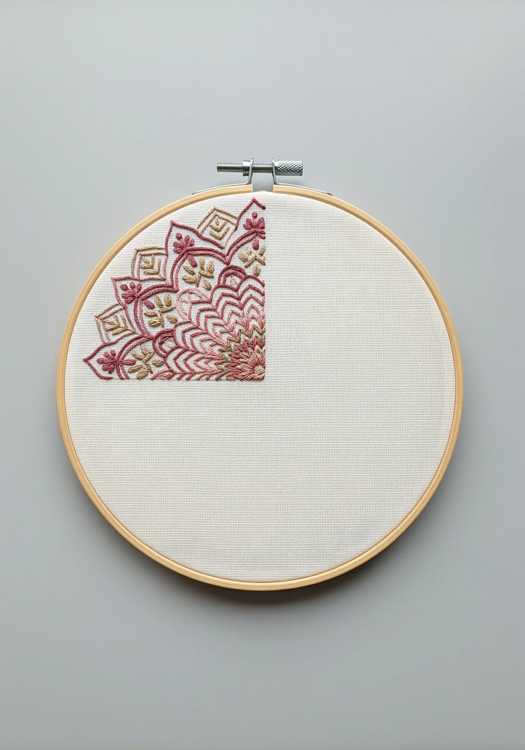 An intricate red and gold mandala stitched only in the top-left corner of a hoop.