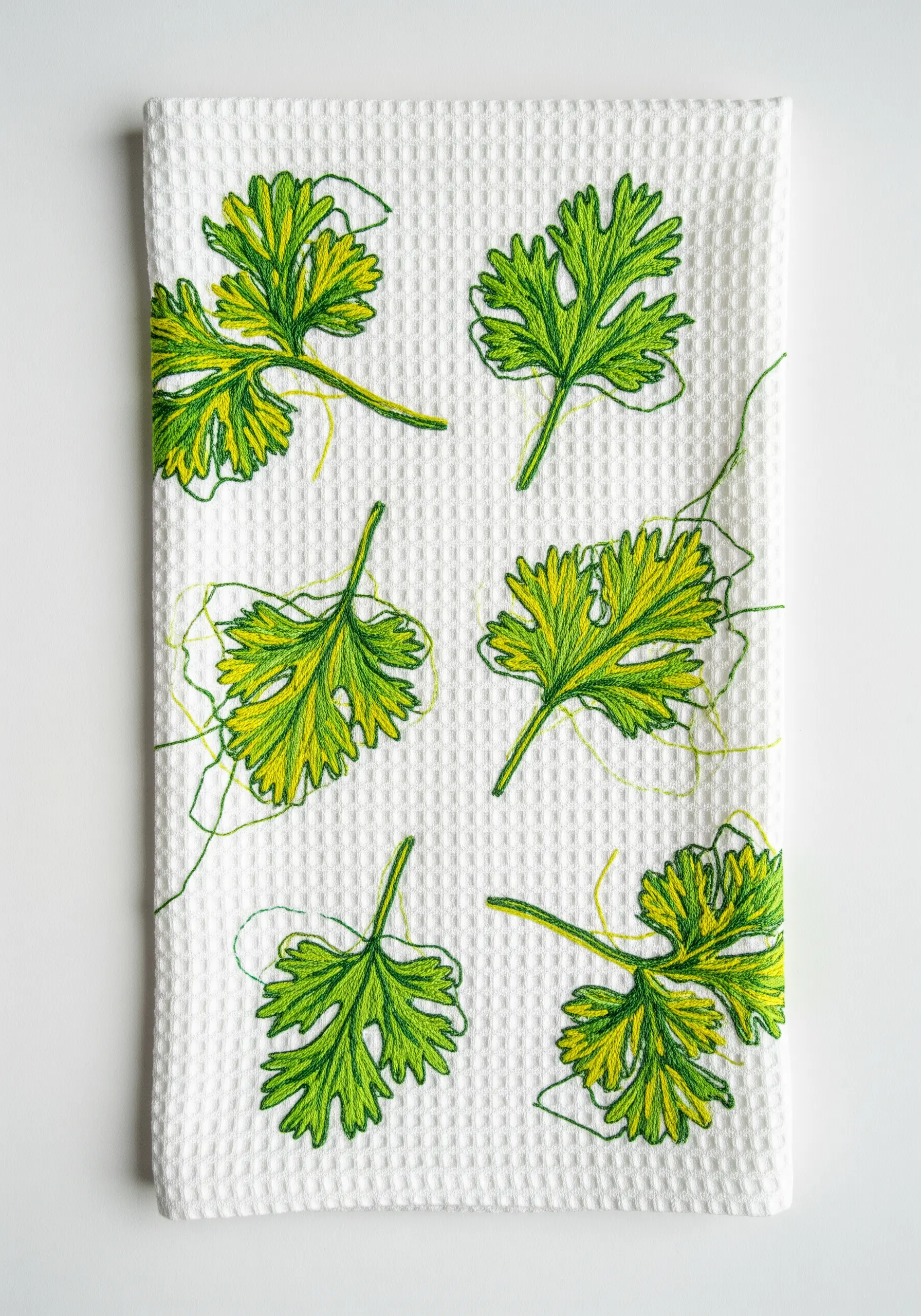 Artistic, sketch-style cilantro leaves with loose threads on a white waffle towel.