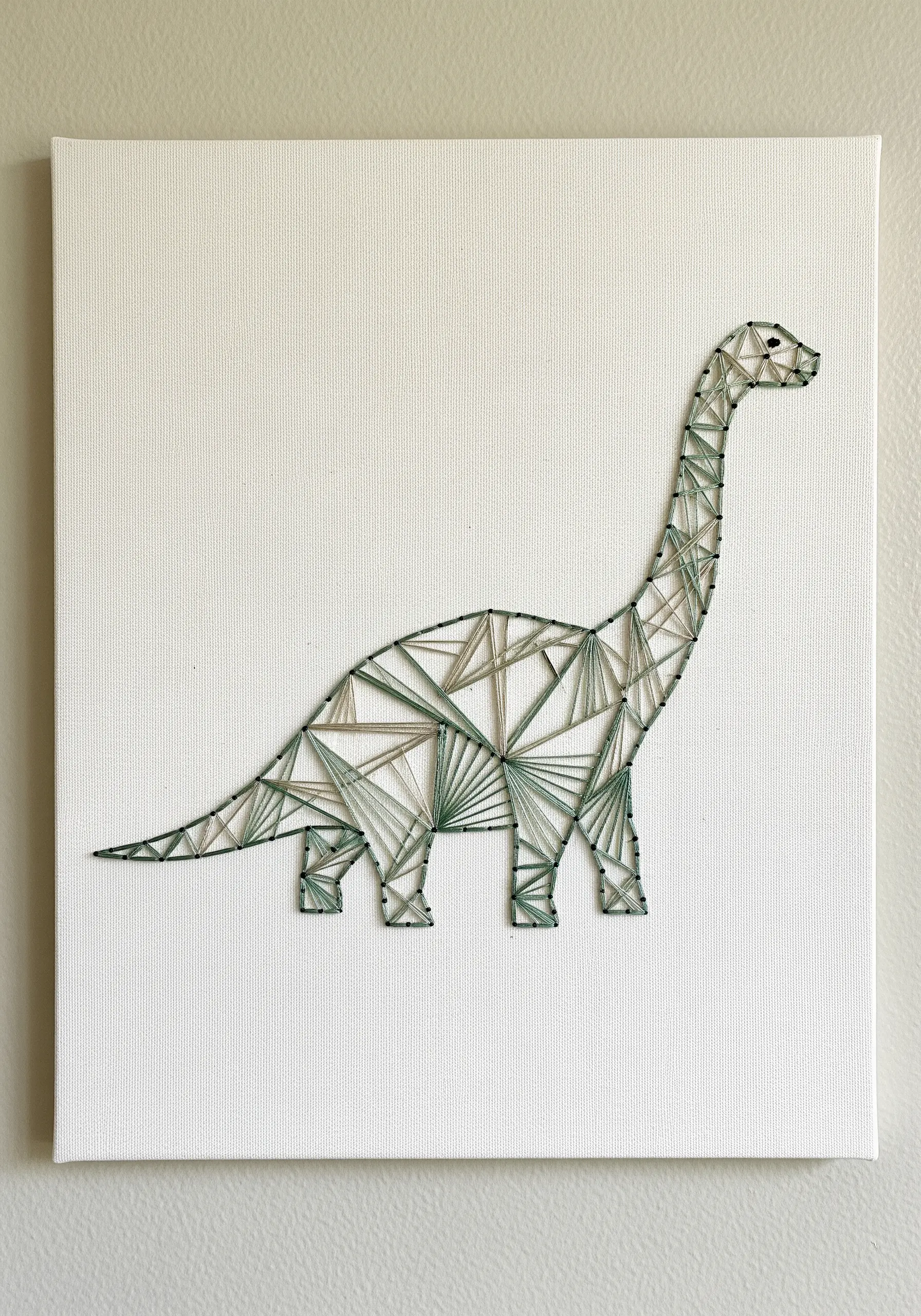 A minimalist brontosaurus created with a delicate, open geometric pattern in soft green threads.