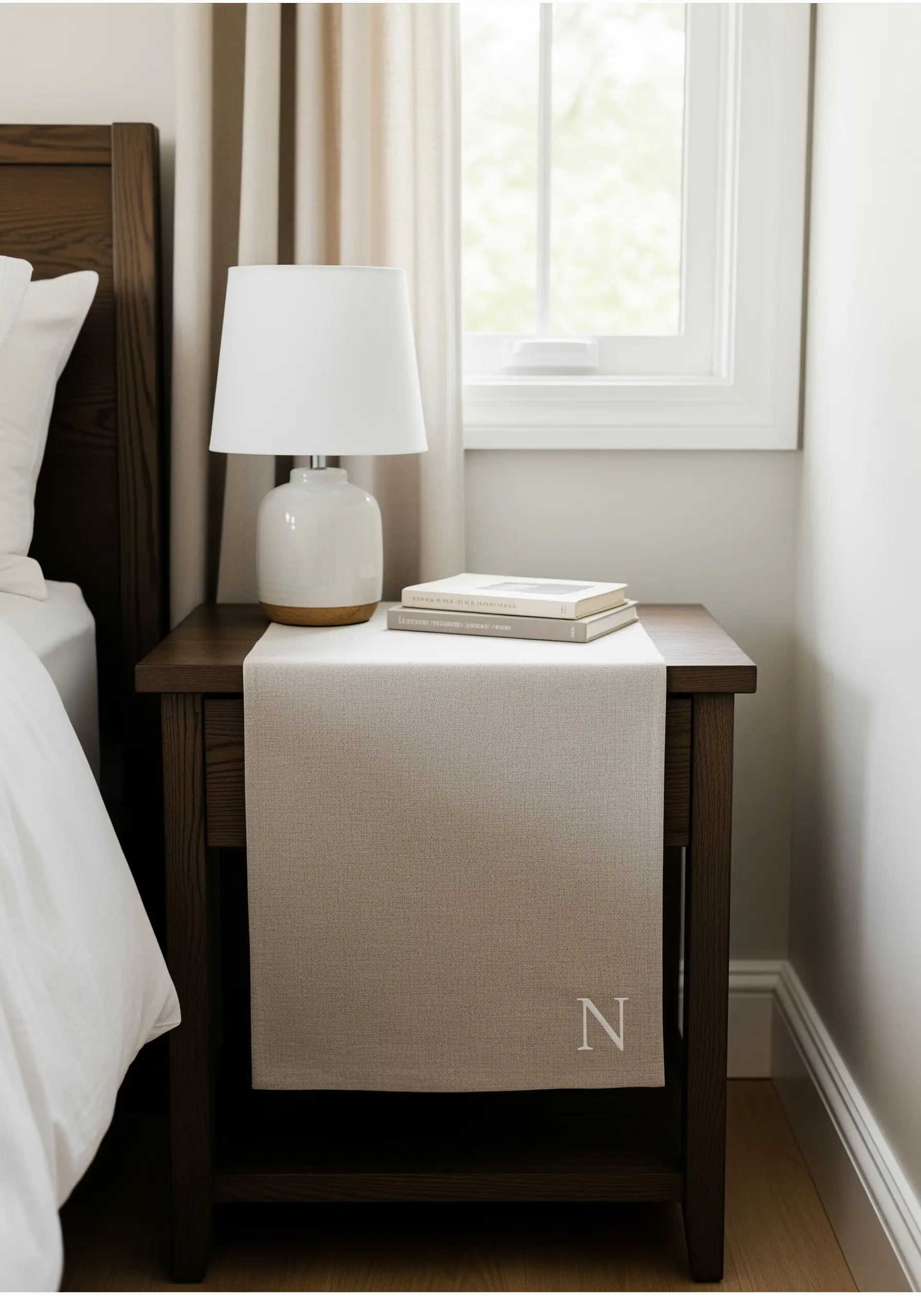 A single white serif initial 'N' embroidered on the corner of a beige bedside table runner.
