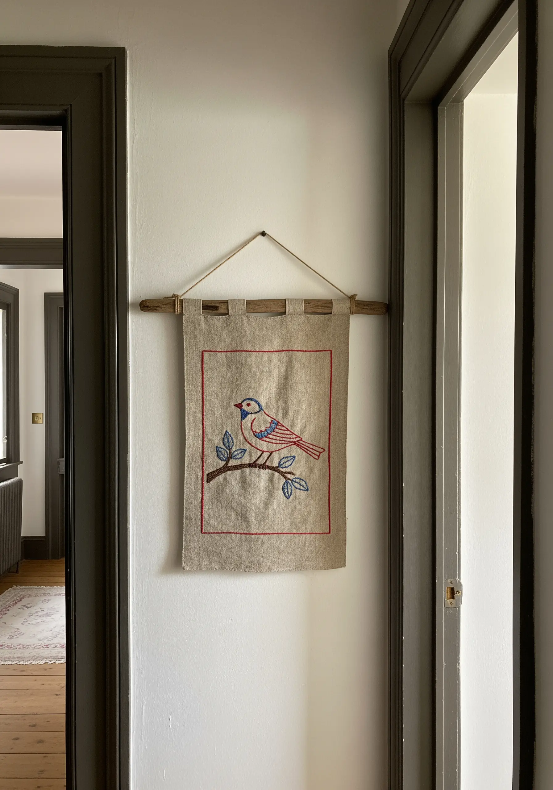 A folk-art style bird embroidered on a simple linen banner with a red border.