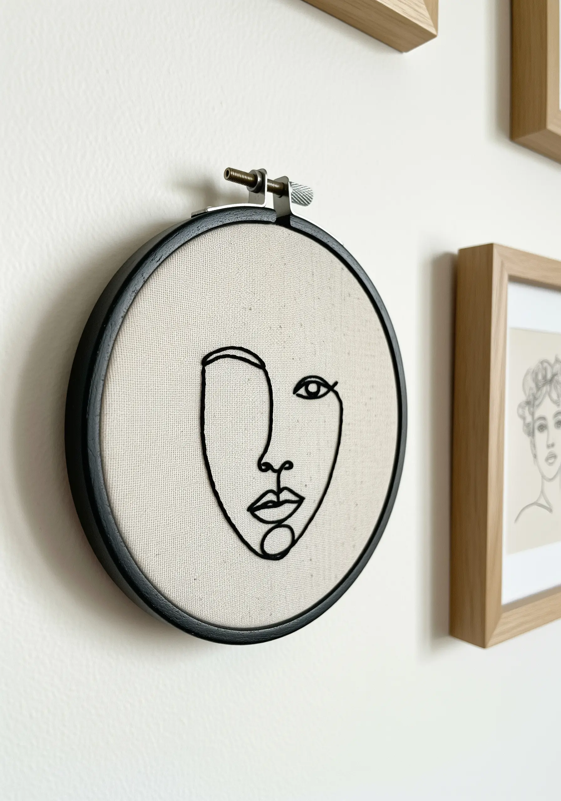 A minimalist line art portrait of a face embroidered in black thread on neutral fabric.