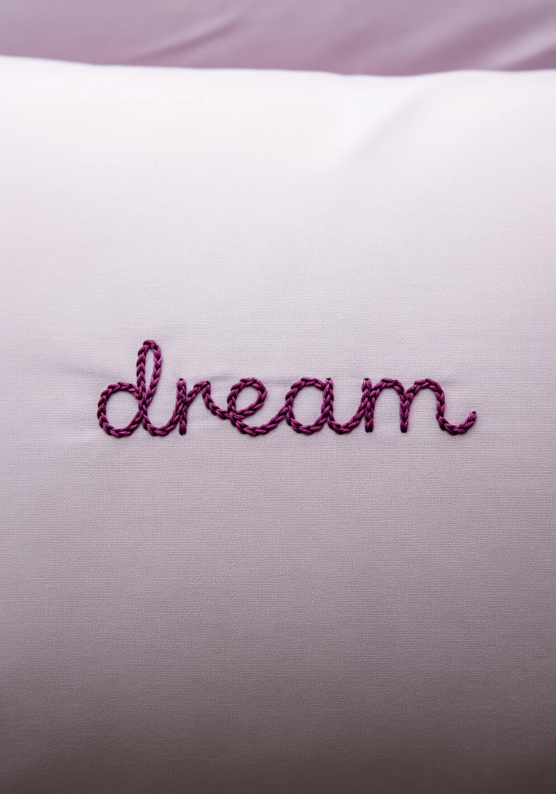 The word 'dream' embroidered in a cursive script with purple thread on a light-colored pillowcase.