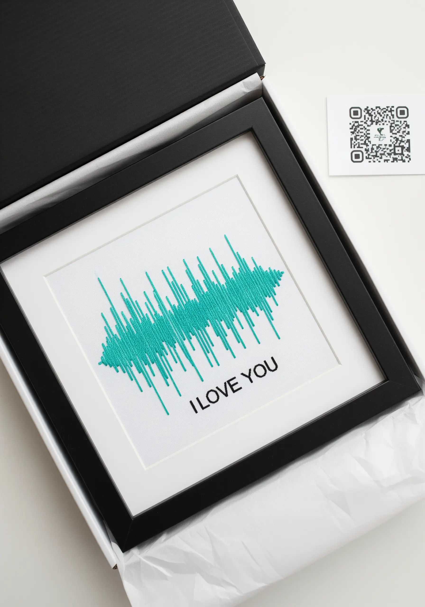 A framed piece of embroidery showing a teal soundwave and the text 'I LOVE YOU'.