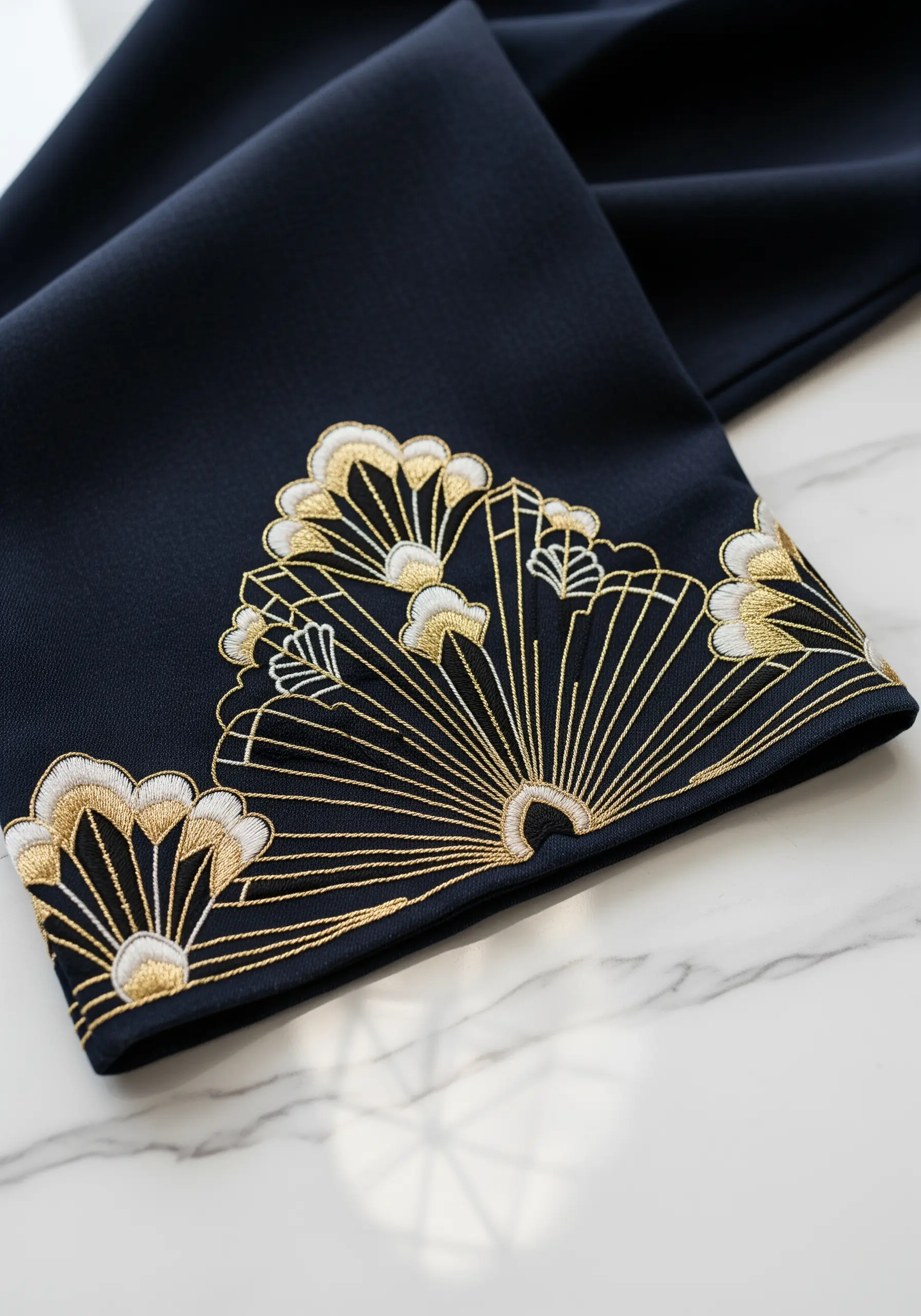 An Art Deco fan design in gold and white thread embroidered on the hem of dark trousers.