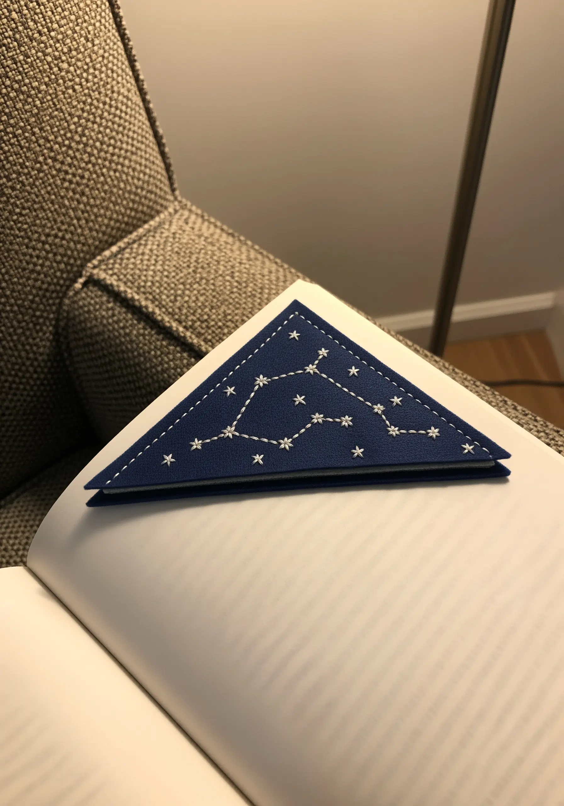 A navy blue faux leather corner bookmark embroidered with a white star constellation.