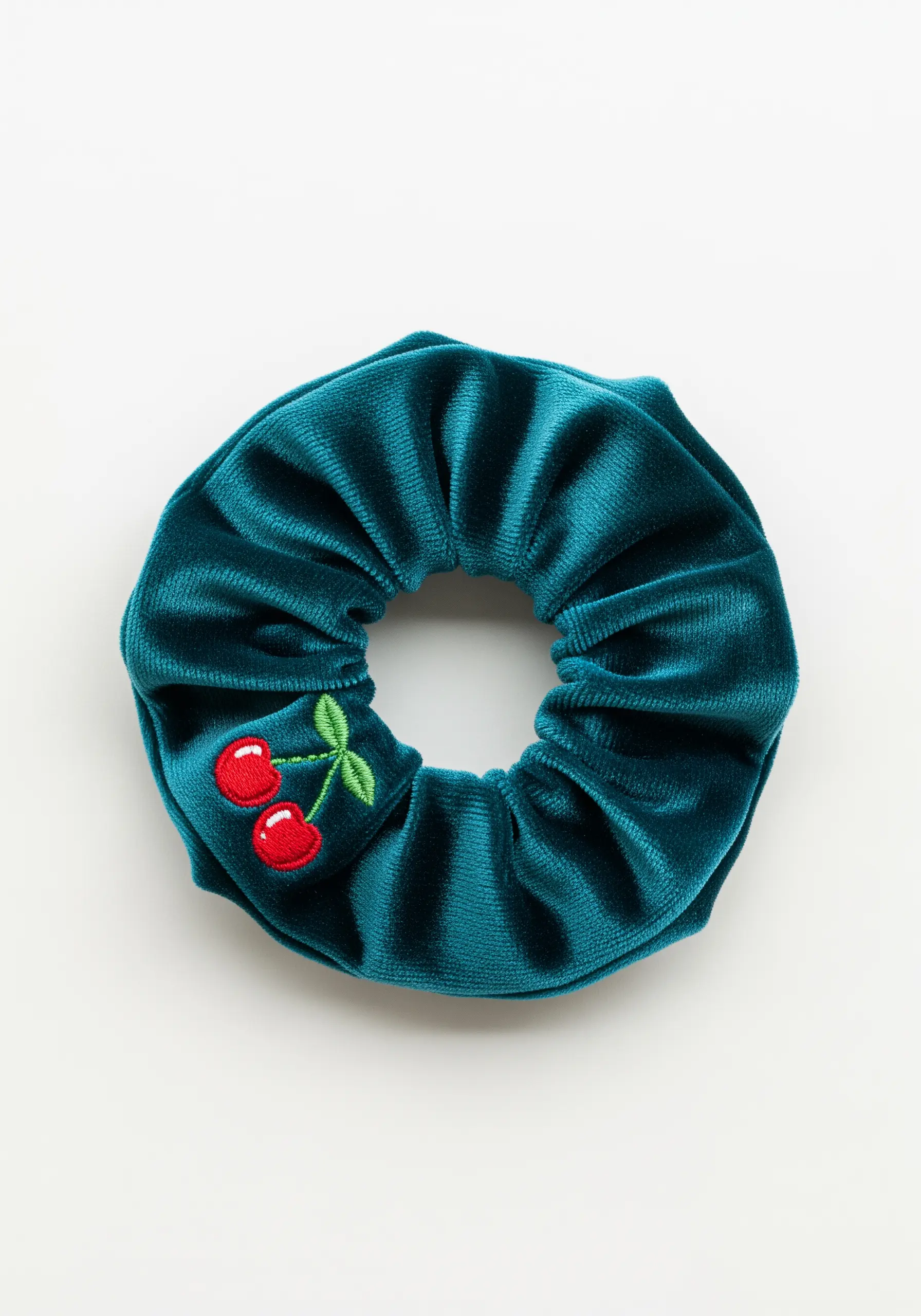 A small pair of red cherries embroidered on a teal velvet scrunchie.