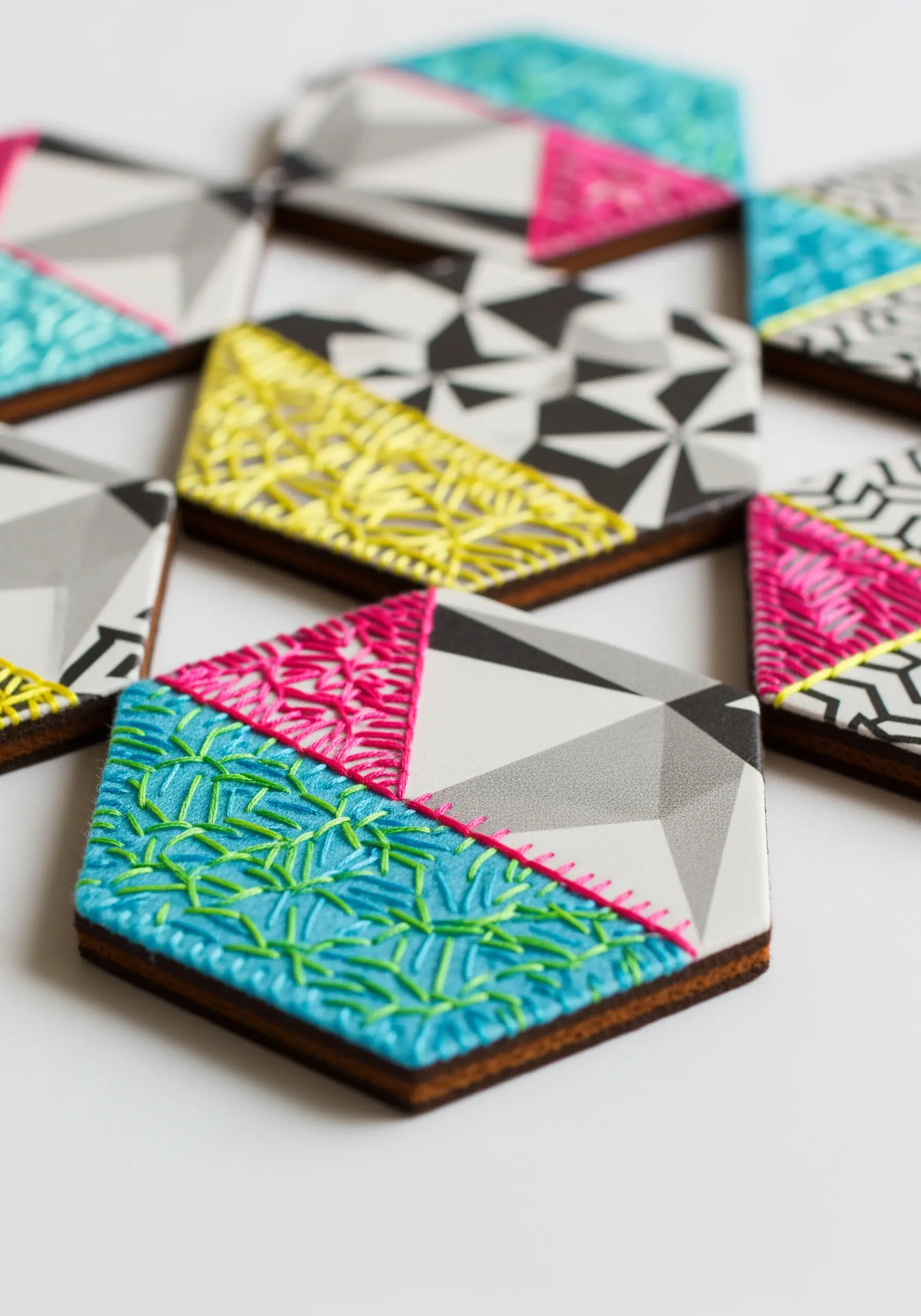 Geometric patterned coasters with sections of bright yellow and blue textural embroidery.