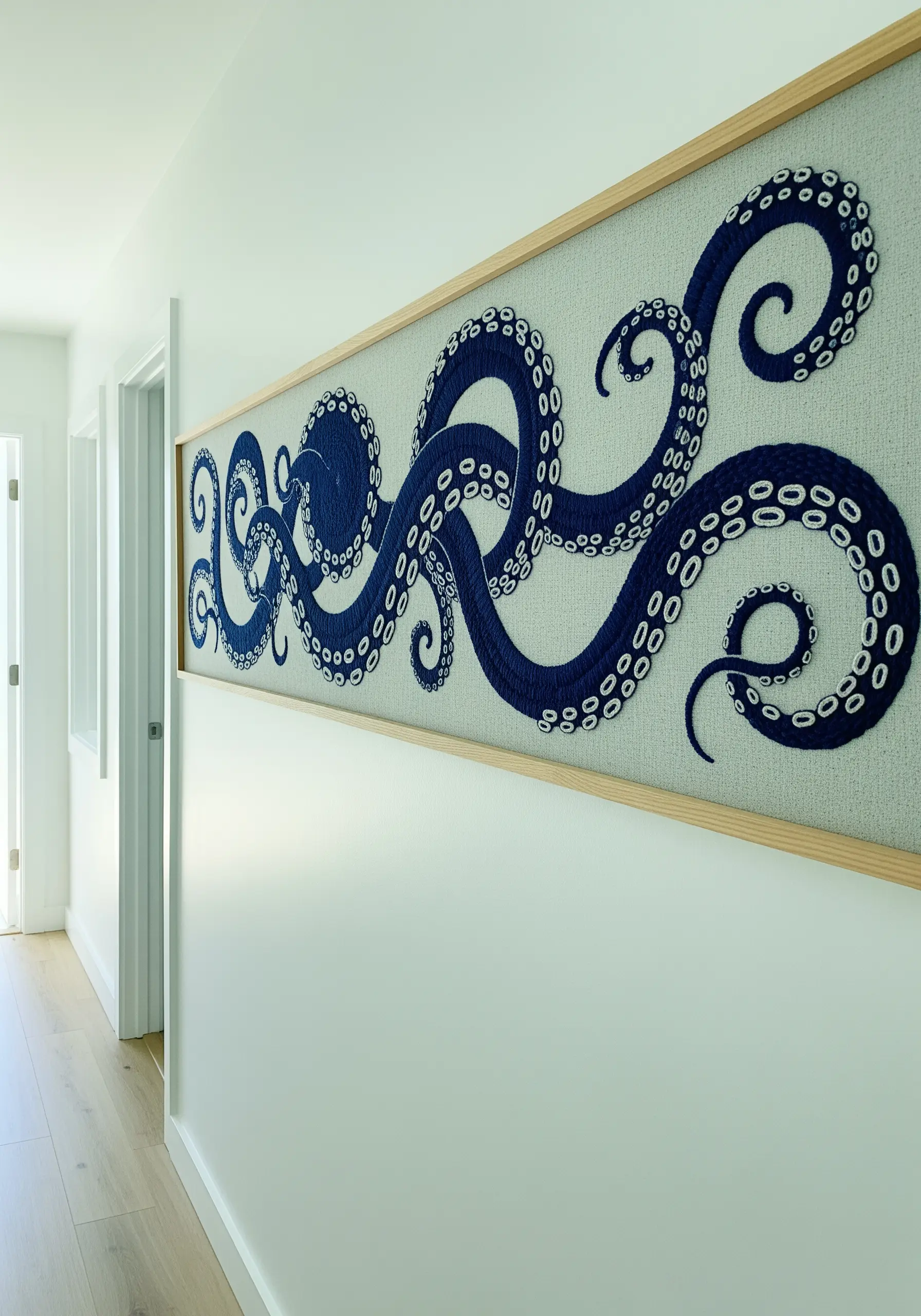 A long, panoramic framed embroidery of dark blue octopus tentacles with white suckers.