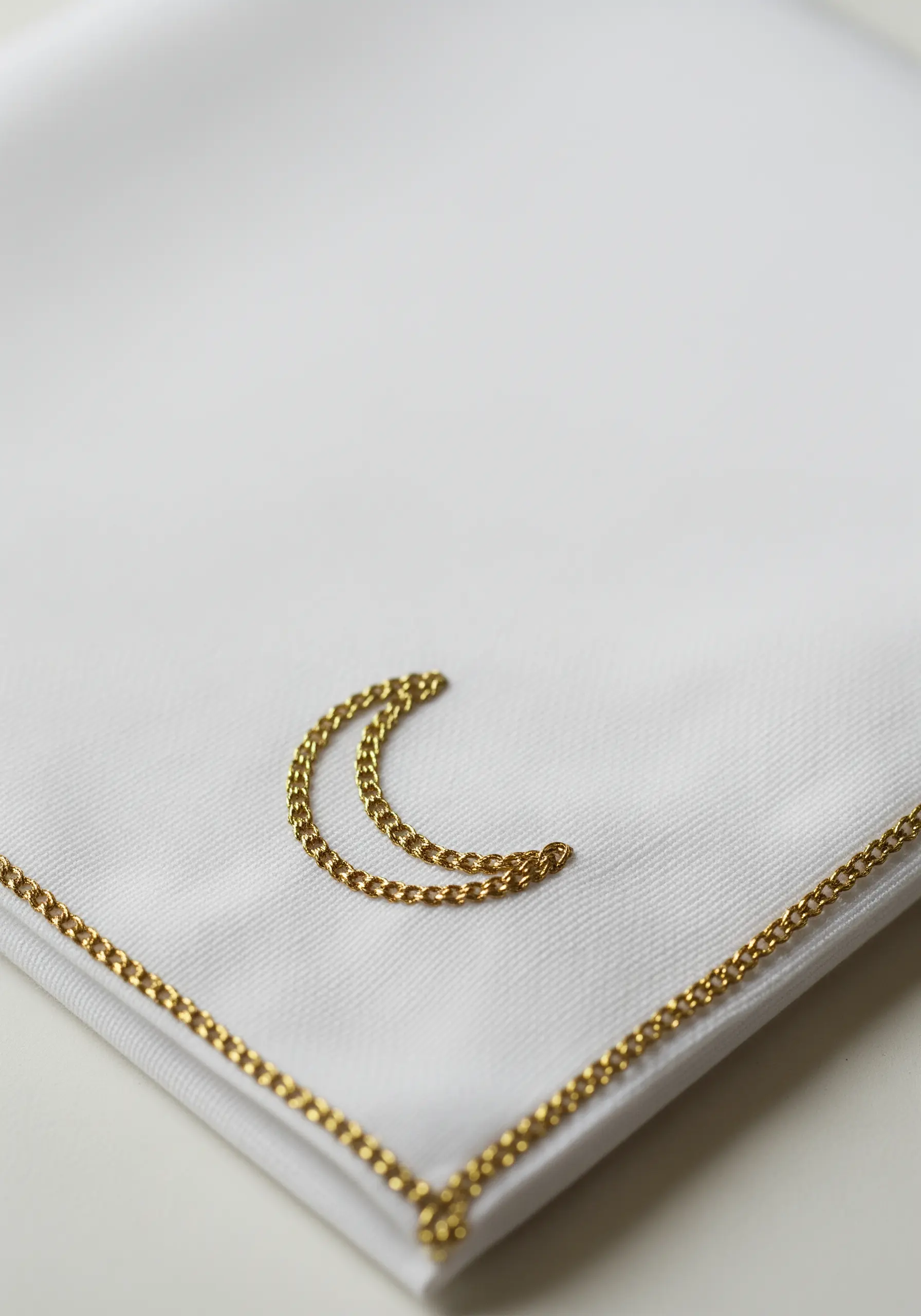 A small crescent moon and border stitched with golden chain stitch on a white handkerchief.