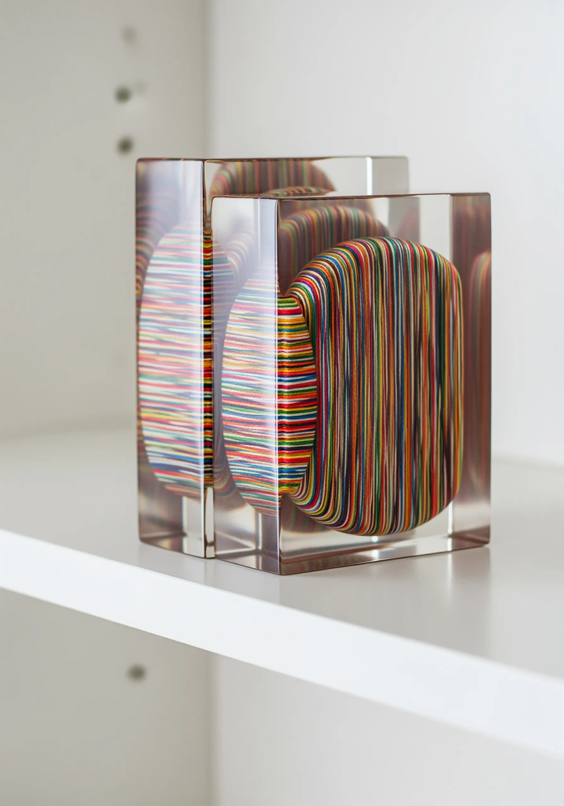 Colorful, tightly wrapped thread forms encased in clear, square resin blocks on a shelf.