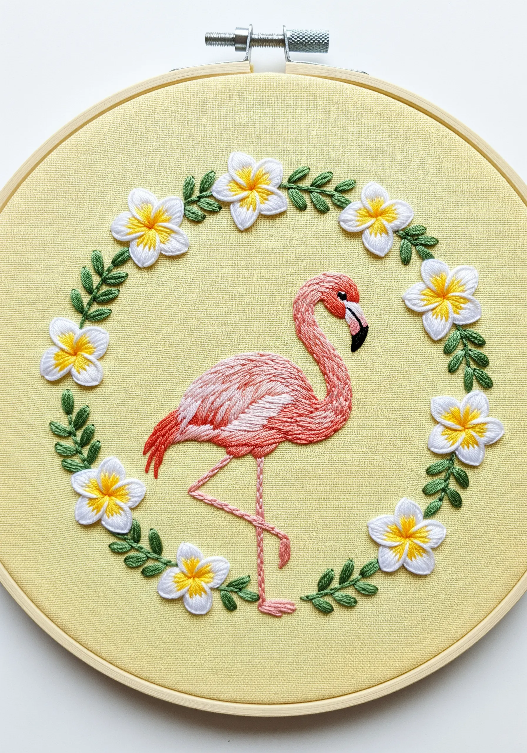 Embroidered flamingo in the center of a floral wreath of plumeria on yellow fabric.