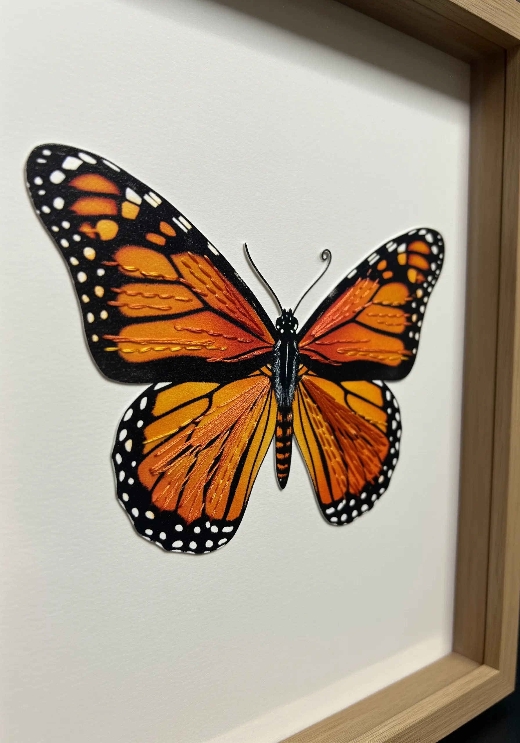 A realistic 3D embroidered monarch butterfly with lifted wings, mounted in a frame.