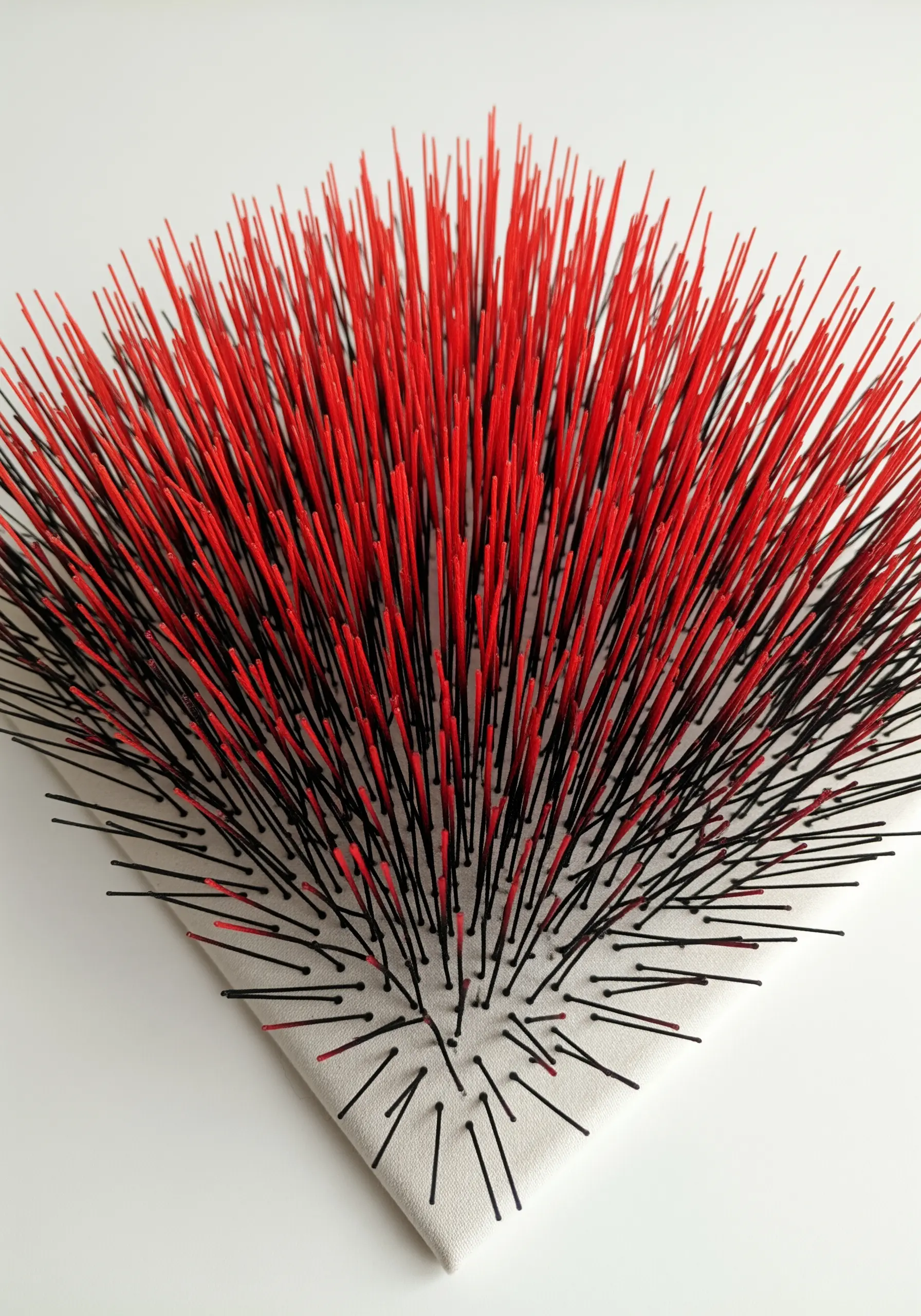 A sculptural piece with sharp red and black spikes of stiffened thread rising from a white canvas.