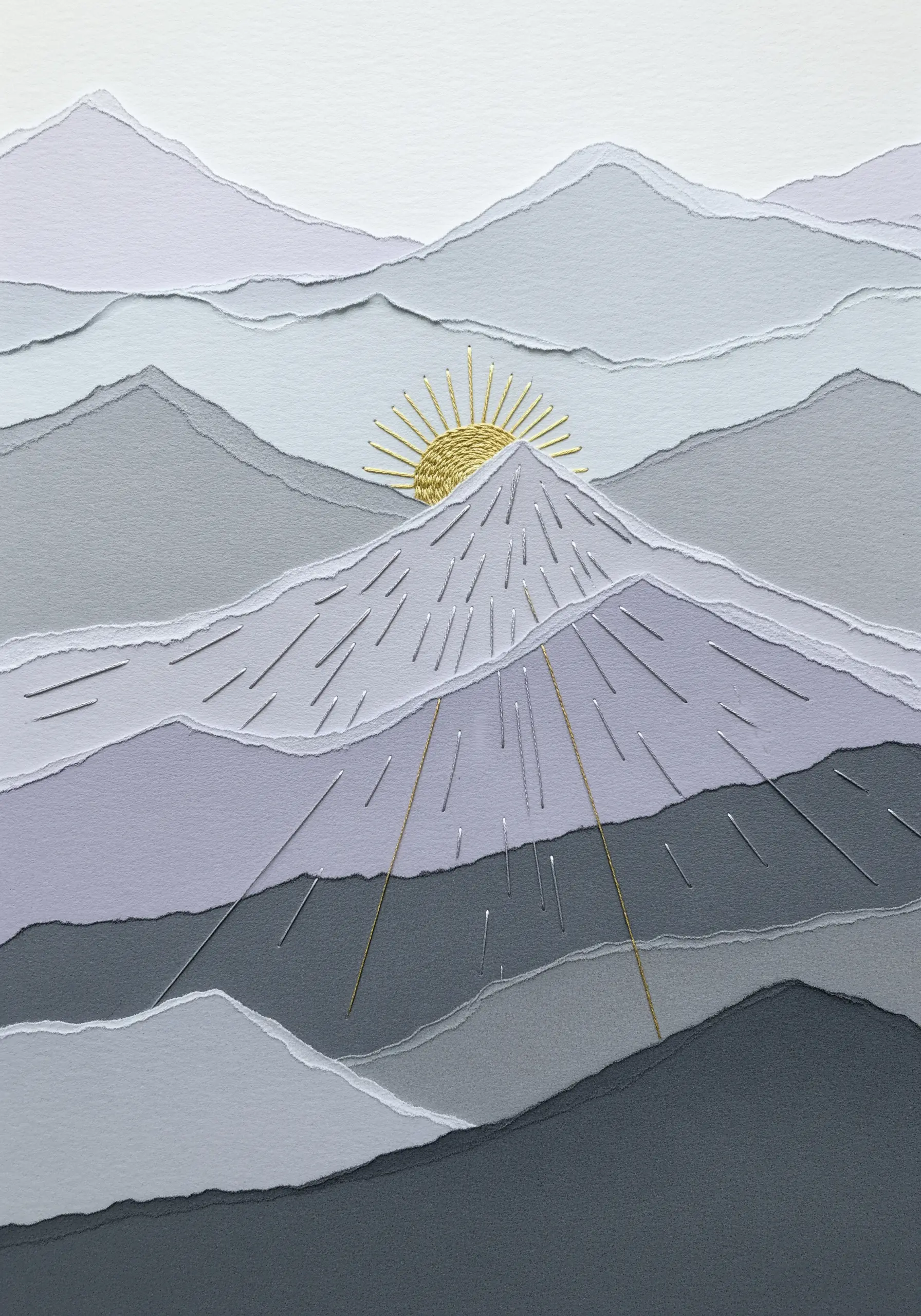 A minimalist mountain landscape made from torn gray paper with an embroidered gold sunburst.