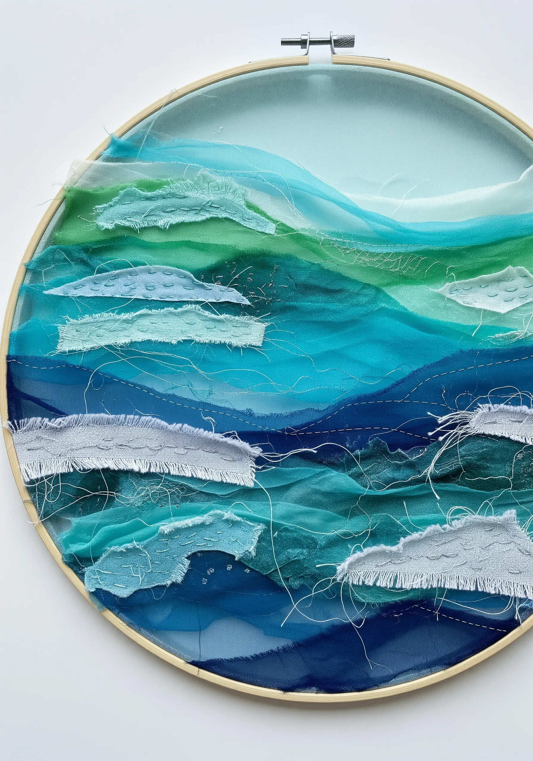 Hoop art seascape made with layered sheer and opaque blue and green fabrics.