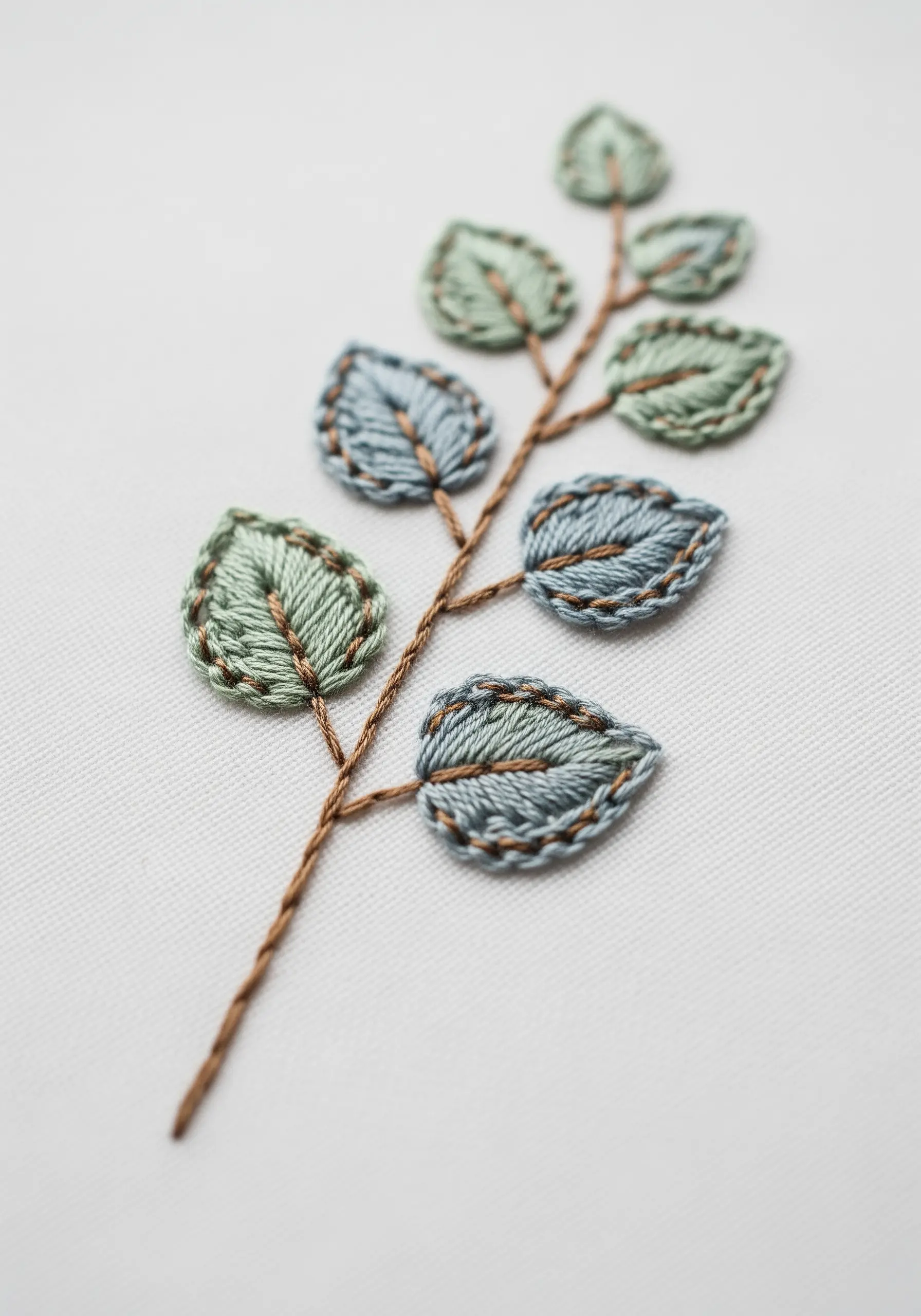 A branch of embroidered eucalyptus leaves with raised, padded satin stitch.