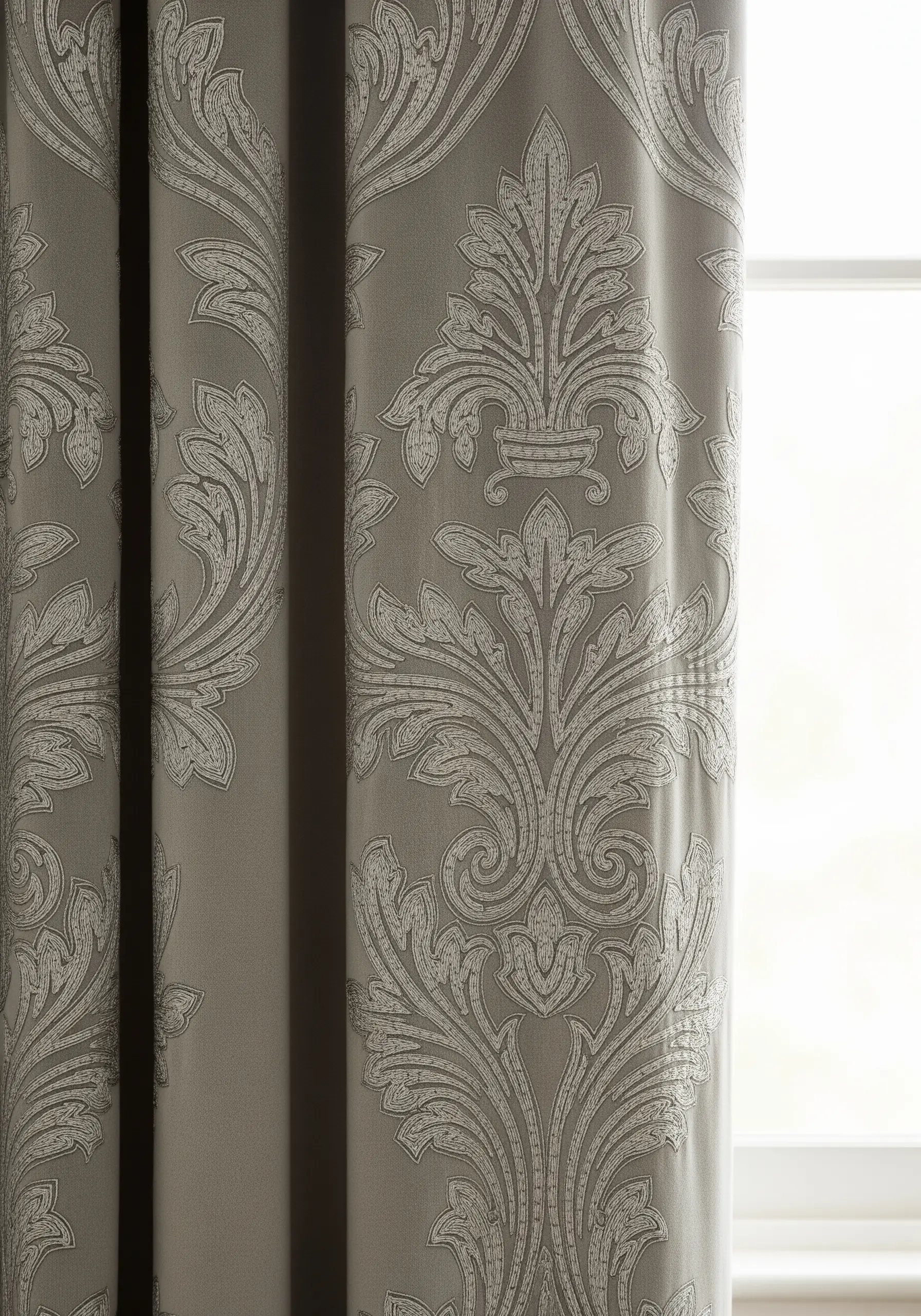 A close-up of a grey curtain with a woven Damask or brocade pattern.