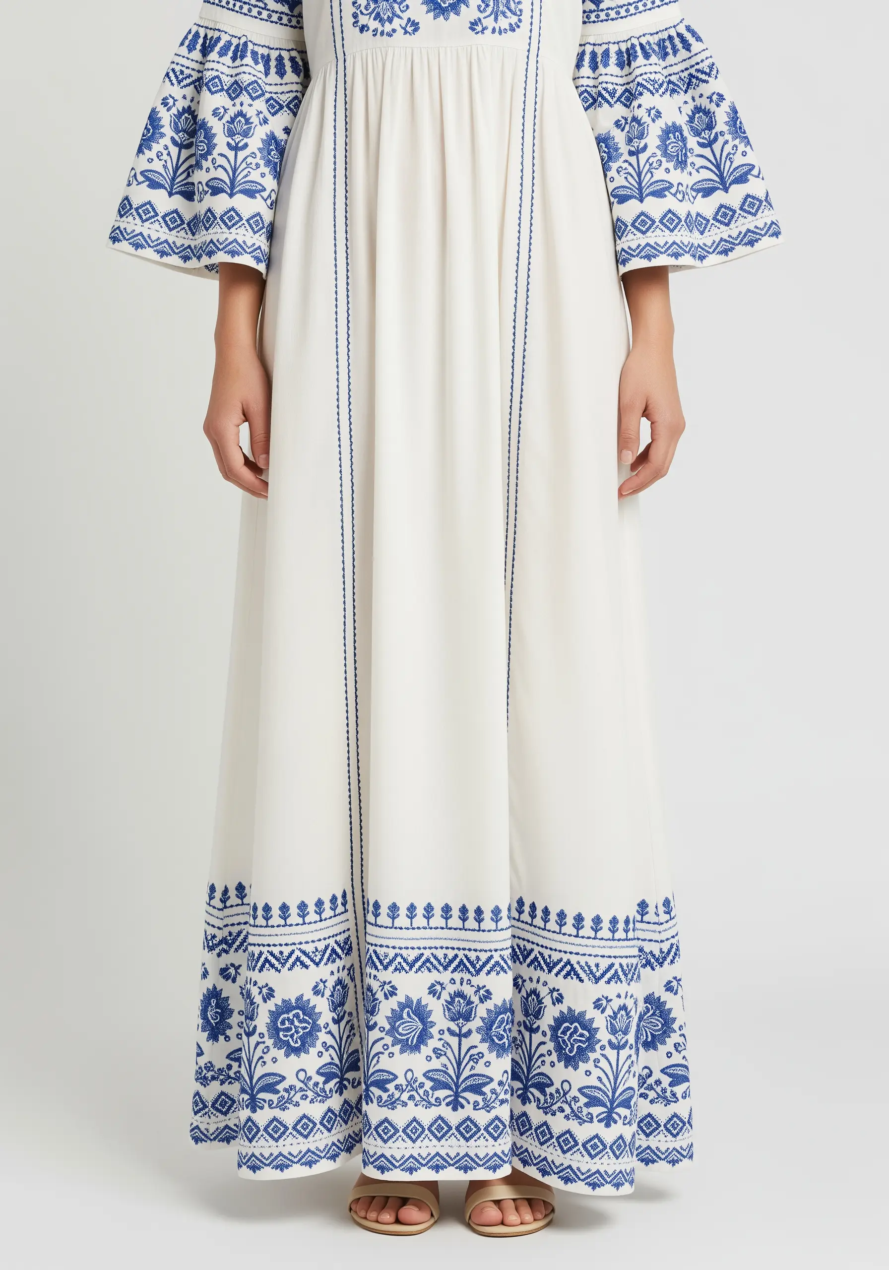 Blue floral and geometric embroidery on the sleeves and hem of a flowing white dress.