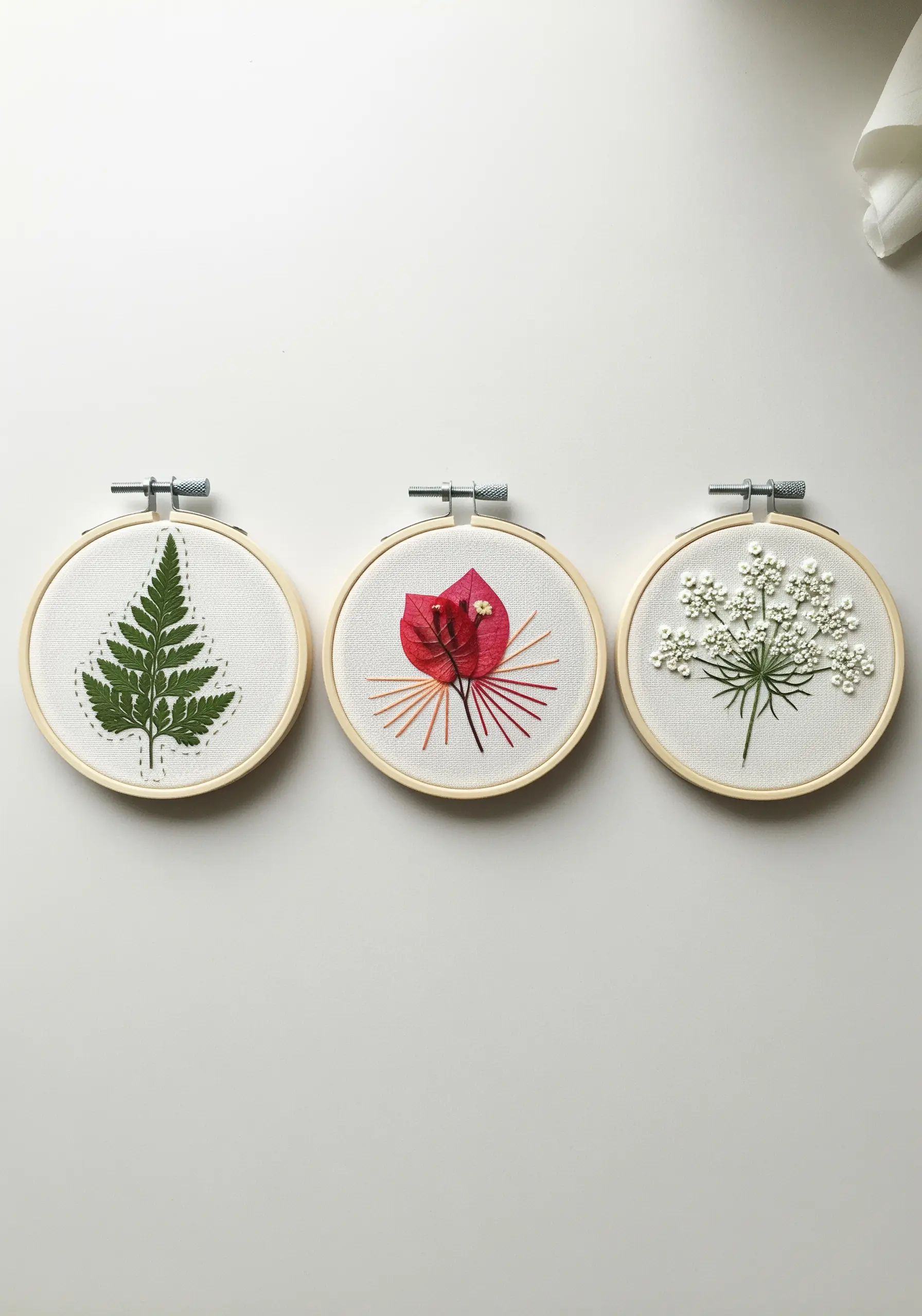 A set of three small embroidery hoops, each featuring a different pressed botanical and stitch style.