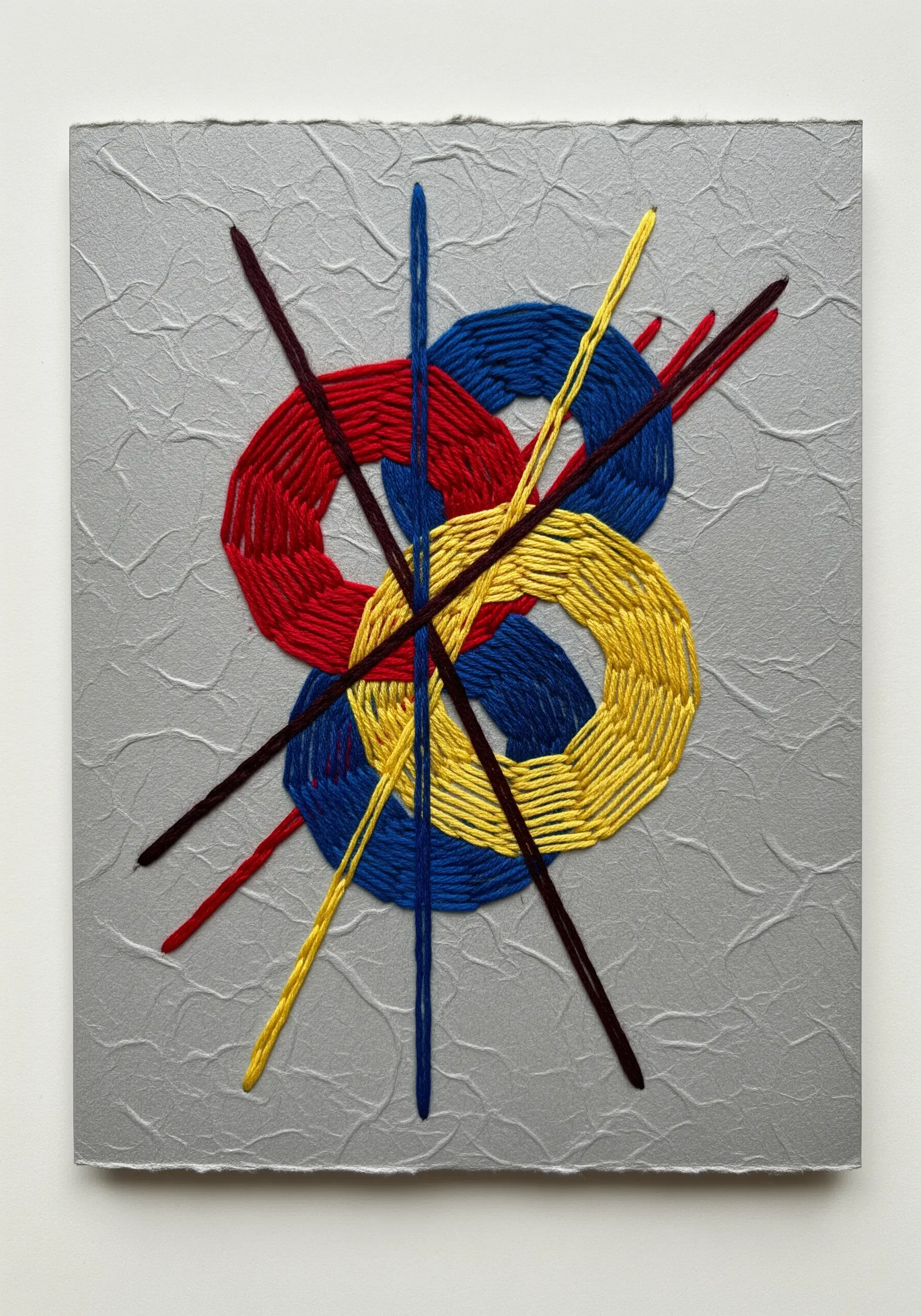Abstract embroidery on textured silver paper with interlocking red, blue, and yellow shapes.