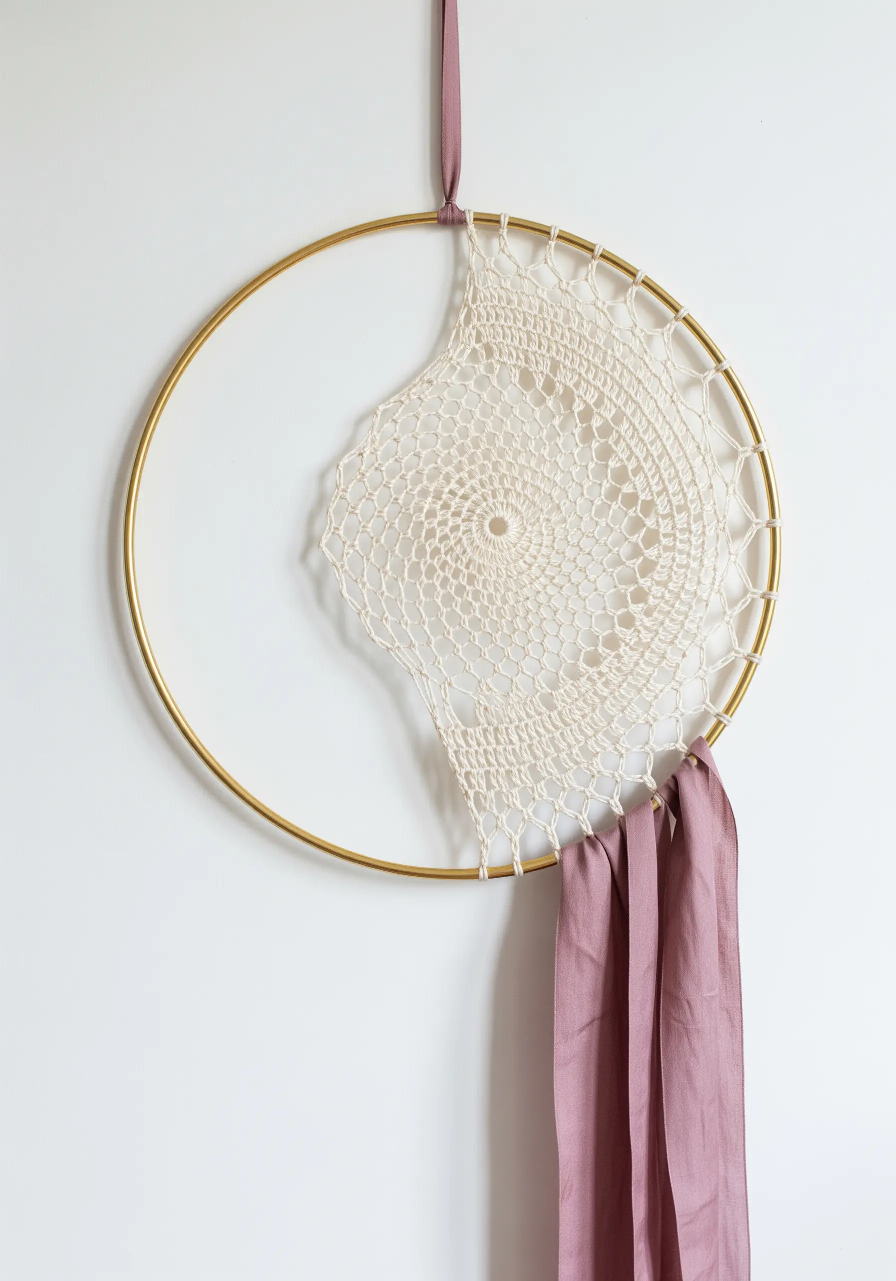A gold hoop with a partial off-center crochet doily and a draped pink silk ribbon.