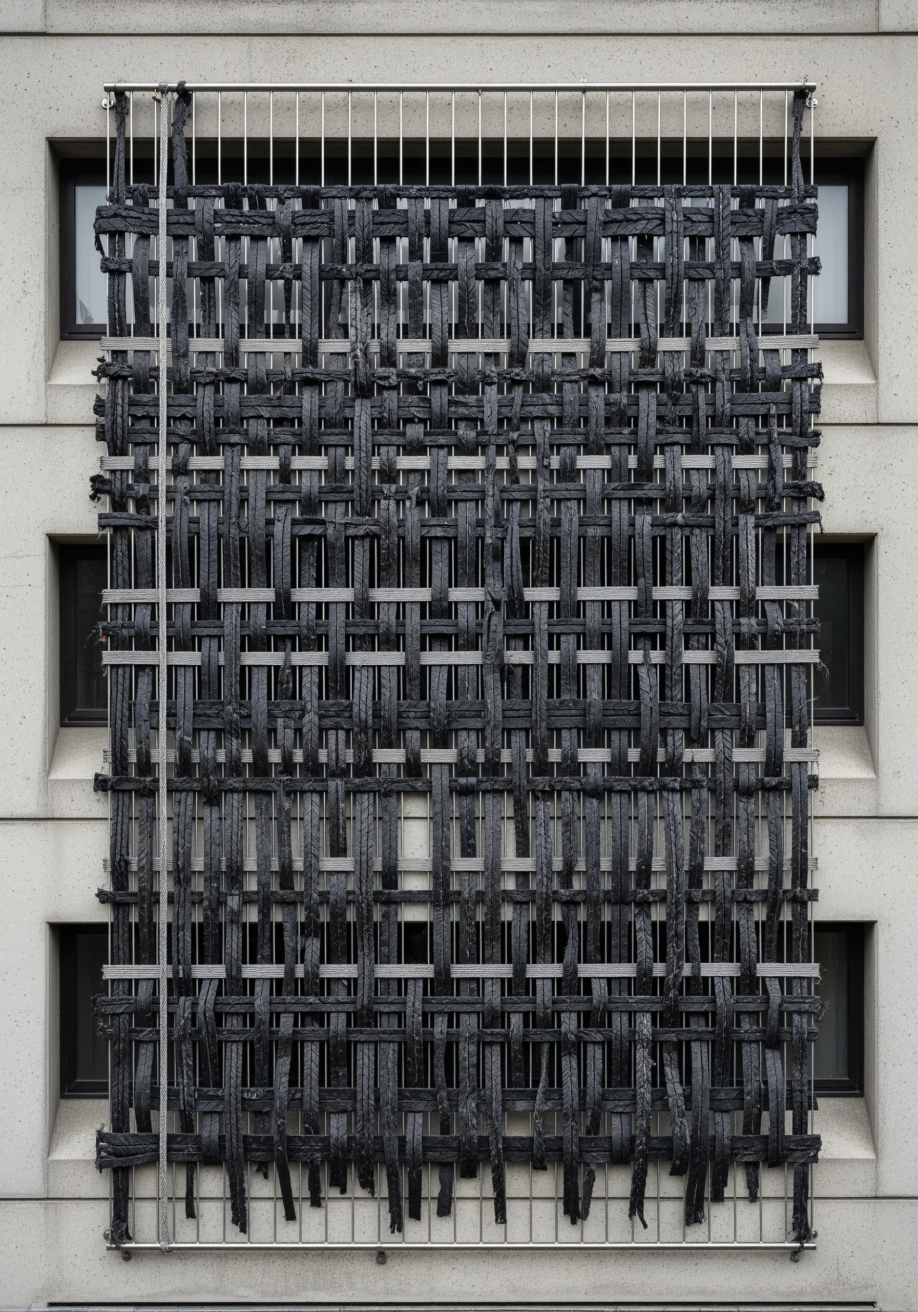 A large-scale woven installation on a building facade made of thick black industrial straps.