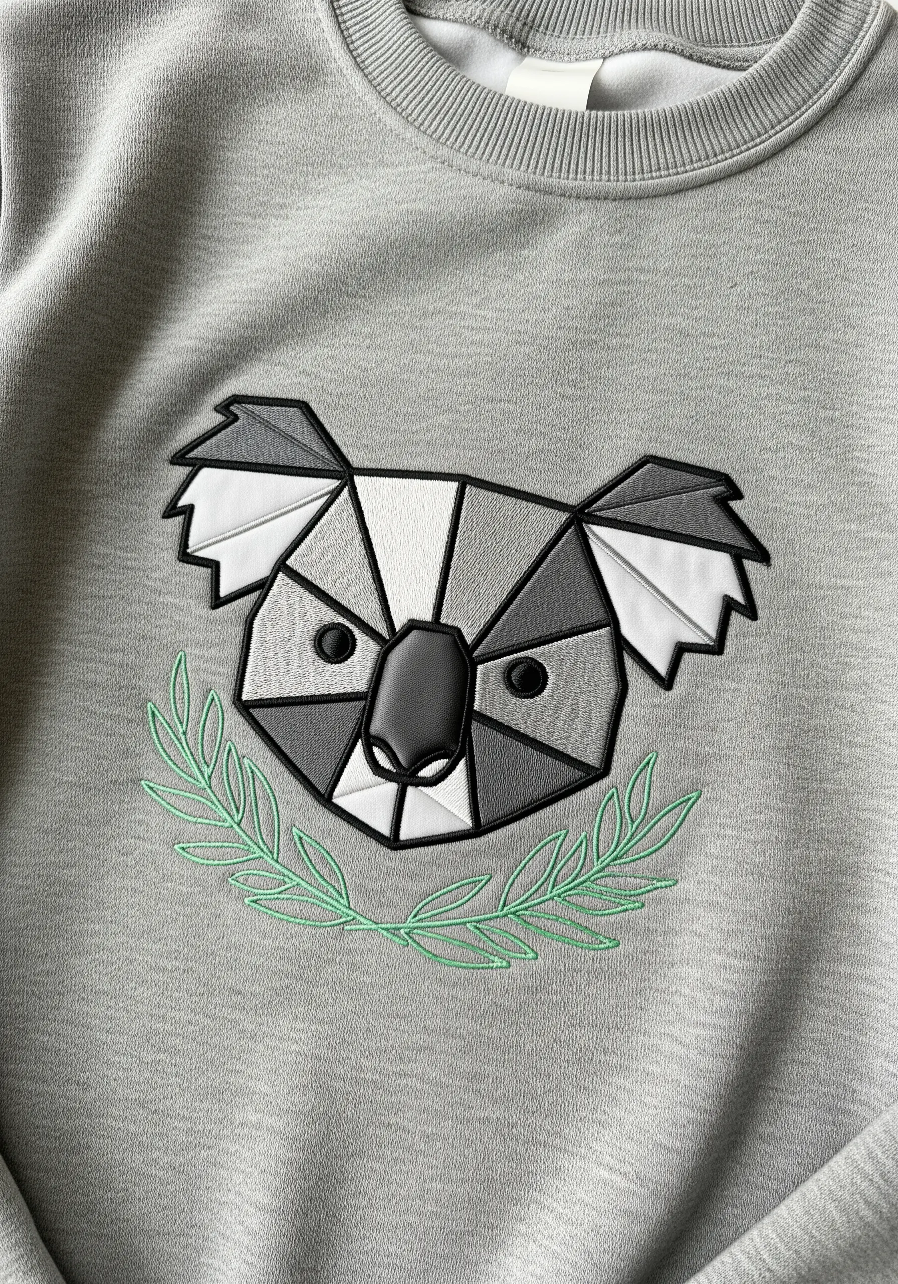 A modern geometric koala face made from faux leather appliqué on a grey sweatshirt.