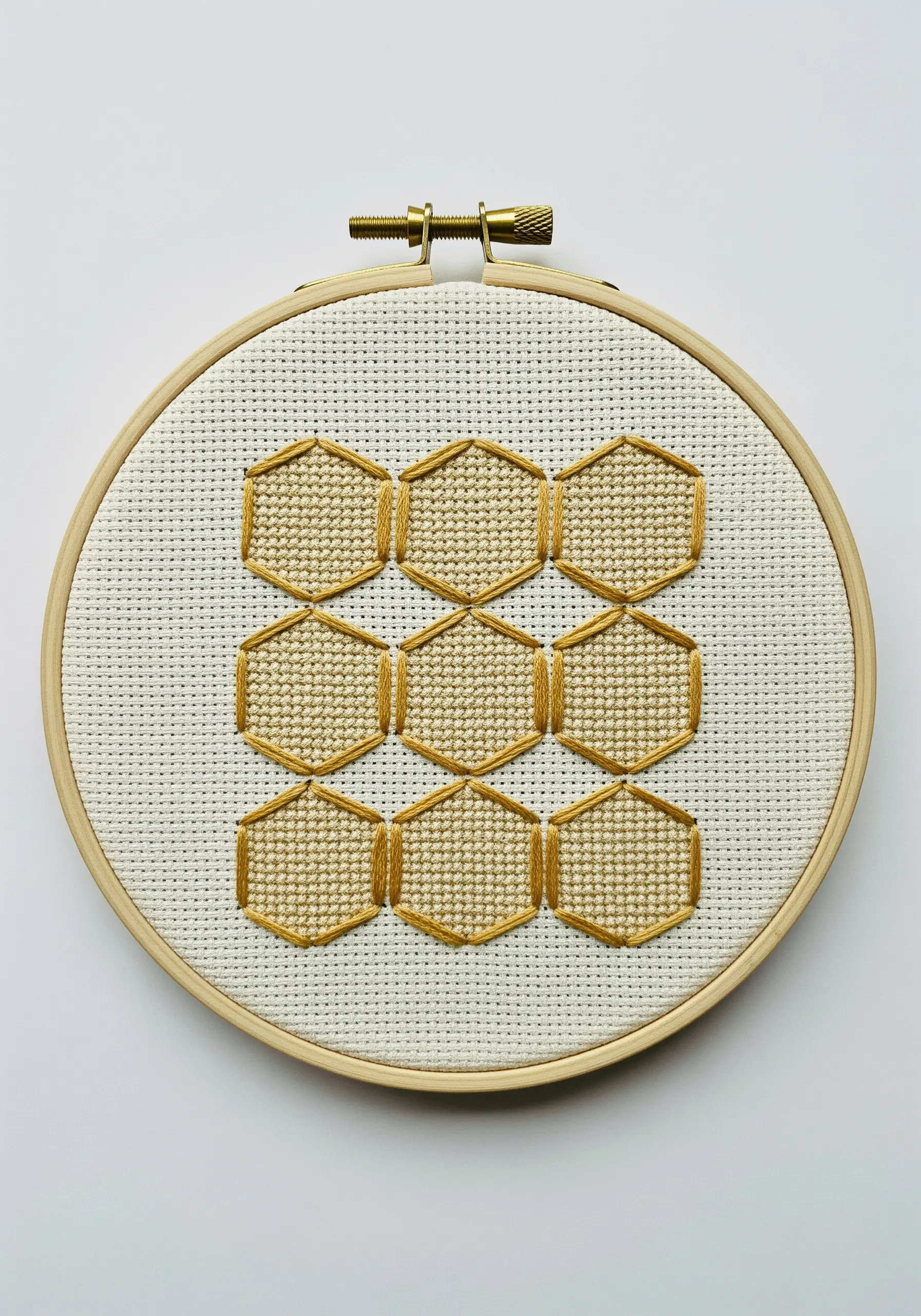A geometric honeycomb pattern with gold outlines and cream-colored fill stitches on Aida cloth.