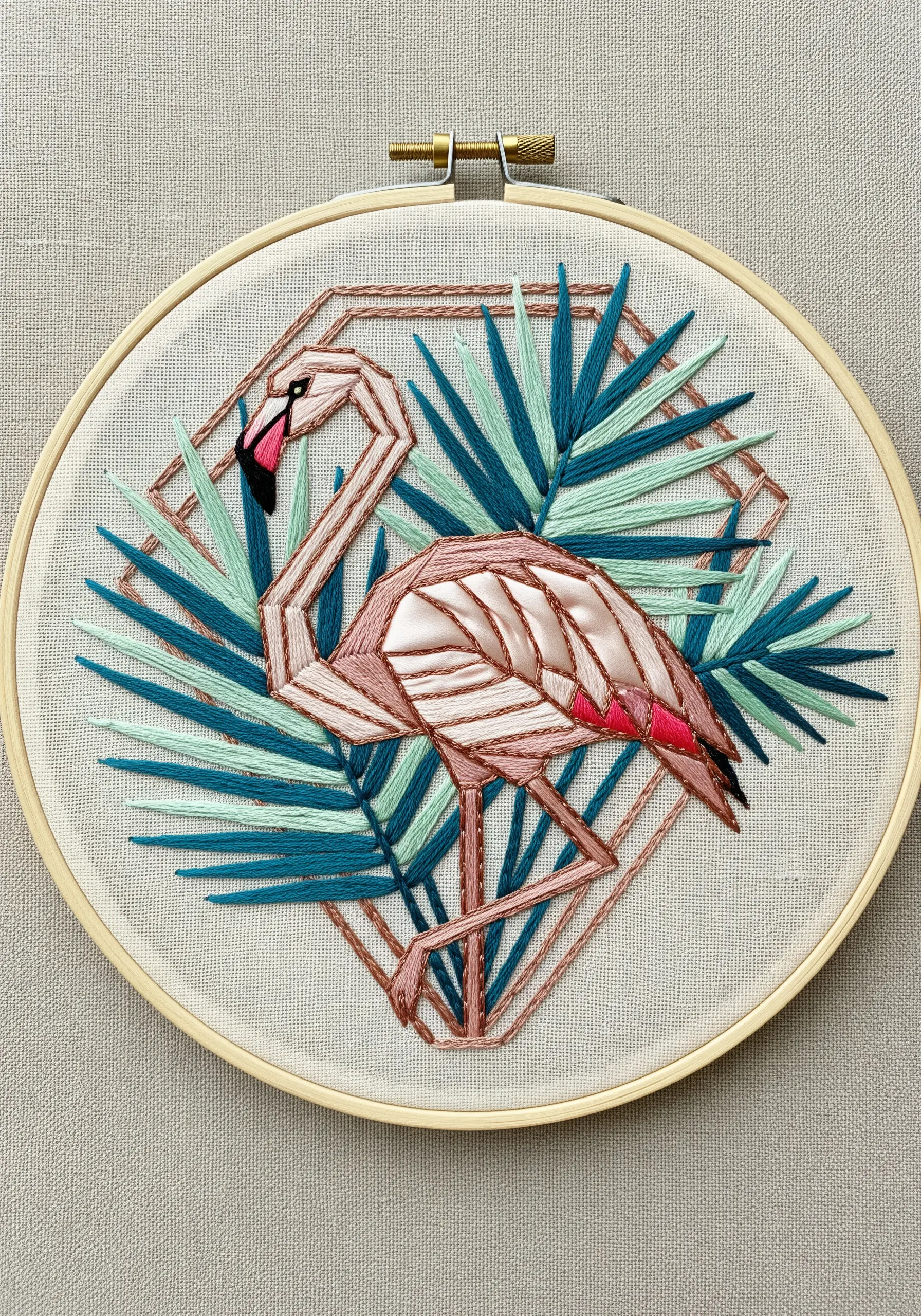 Geometric flamingo with satin-stitched segments in pink and teal in a wooden hoop.