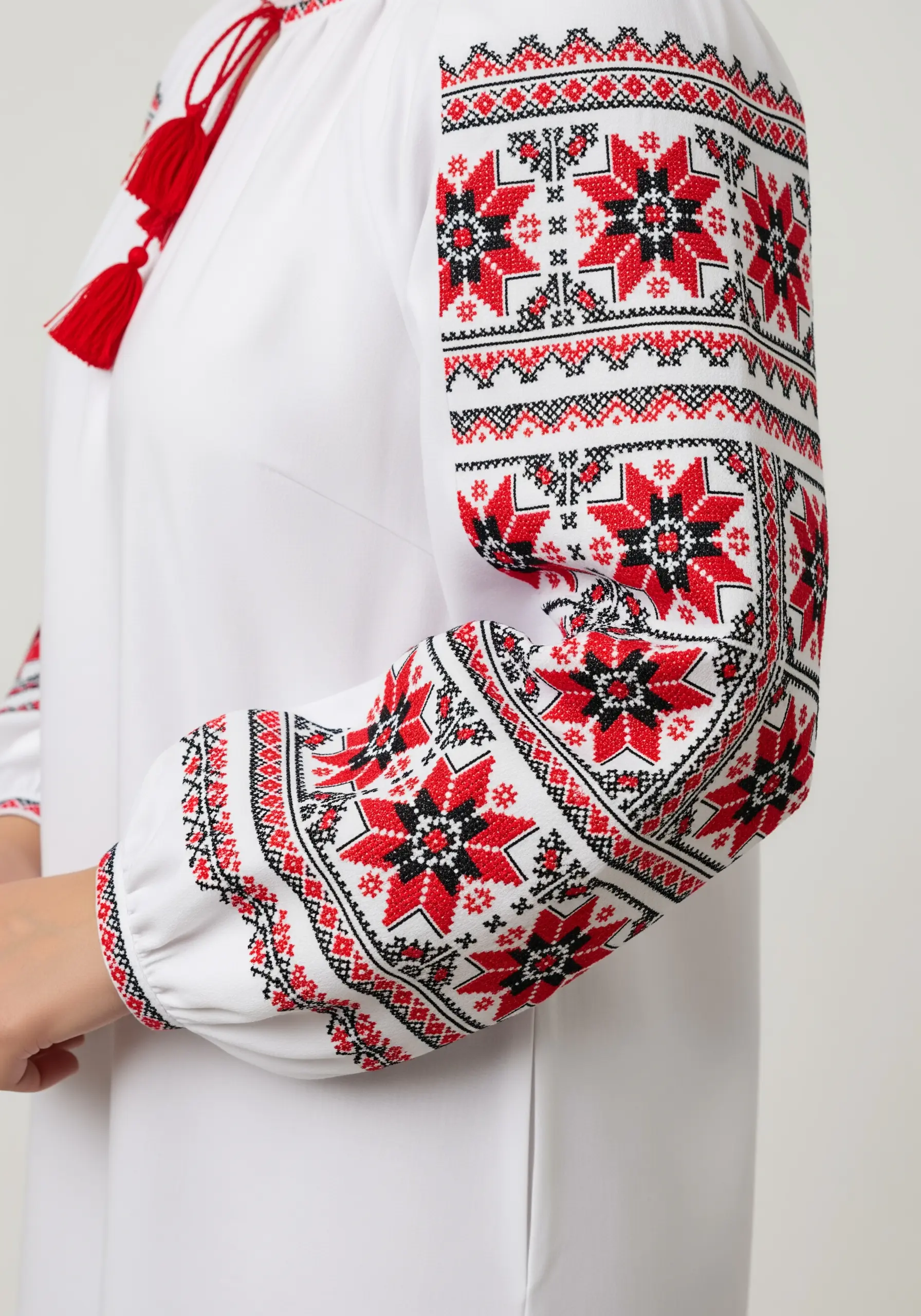 Geometric red and black cross-stitch embroidery on the voluminous sleeve of a white blouse.