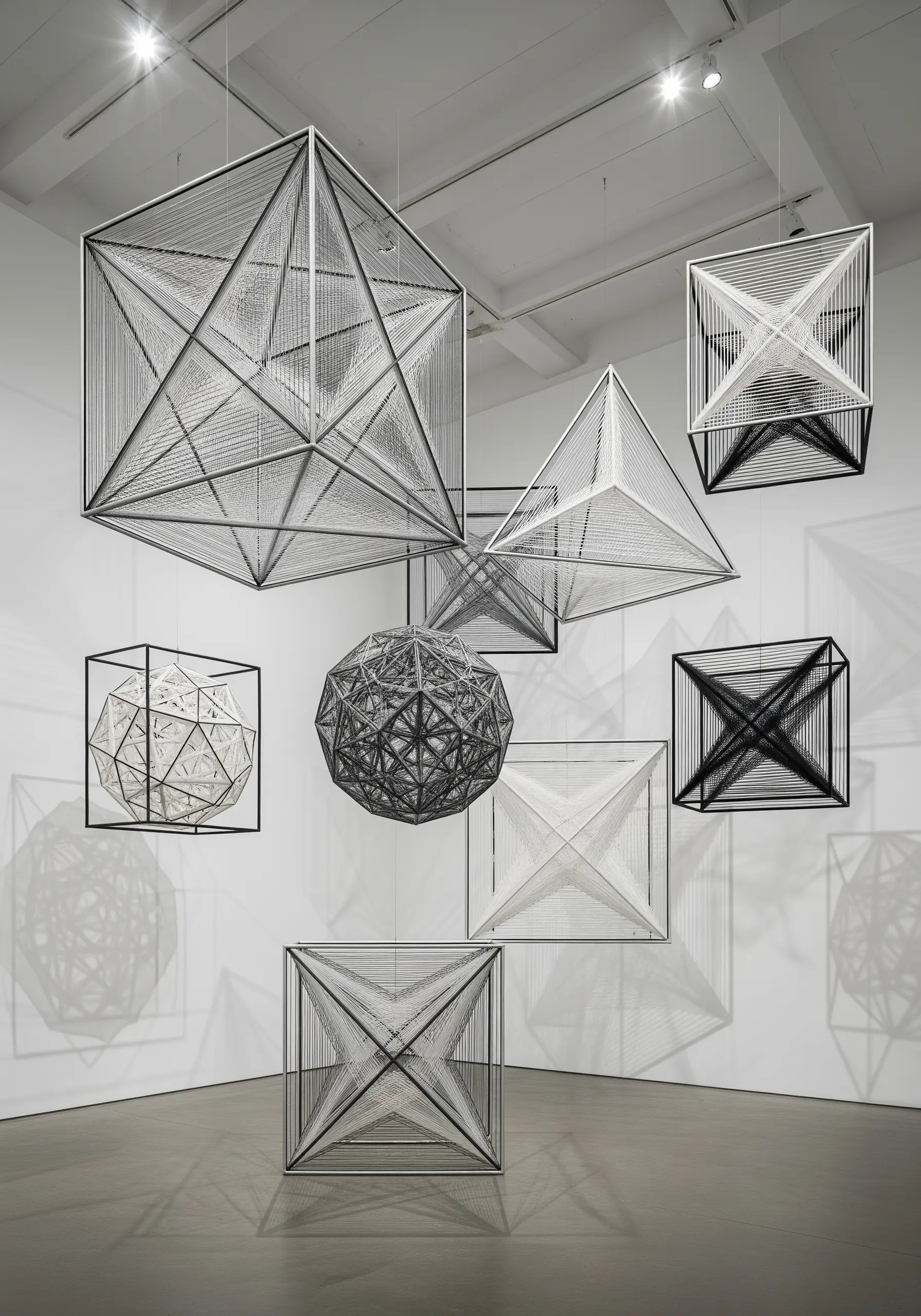 A collection of suspended geometric cubes and spheres made from stretched white and black thread.