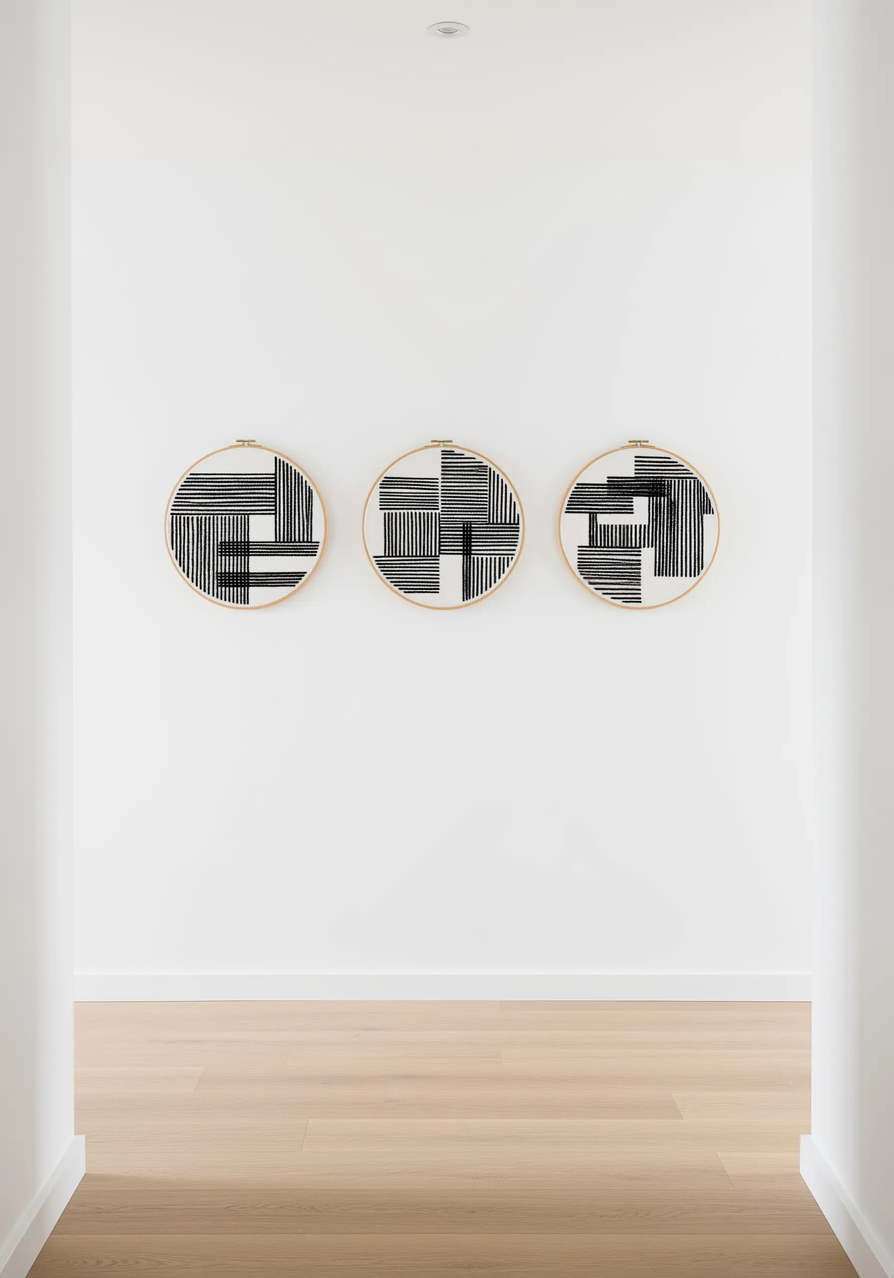Three embroidery hoops with abstract black-and-white geometric patterns made of straight stitches.