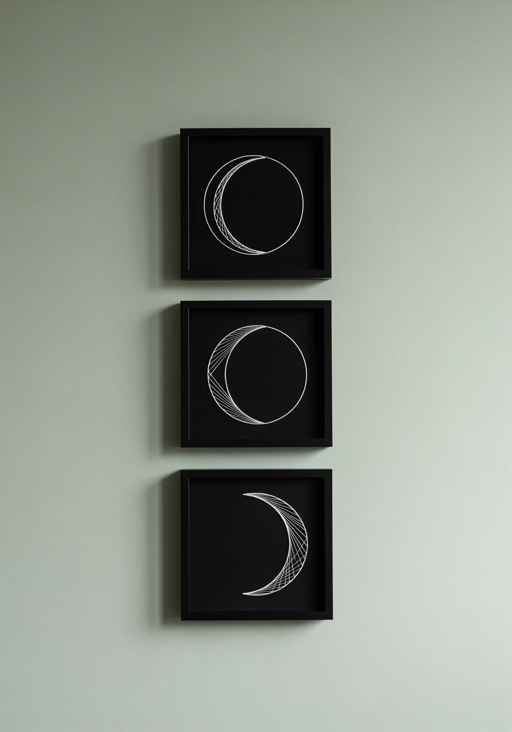 A set of three framed embroideries showing the phases of the moon in white thread on black fabric.