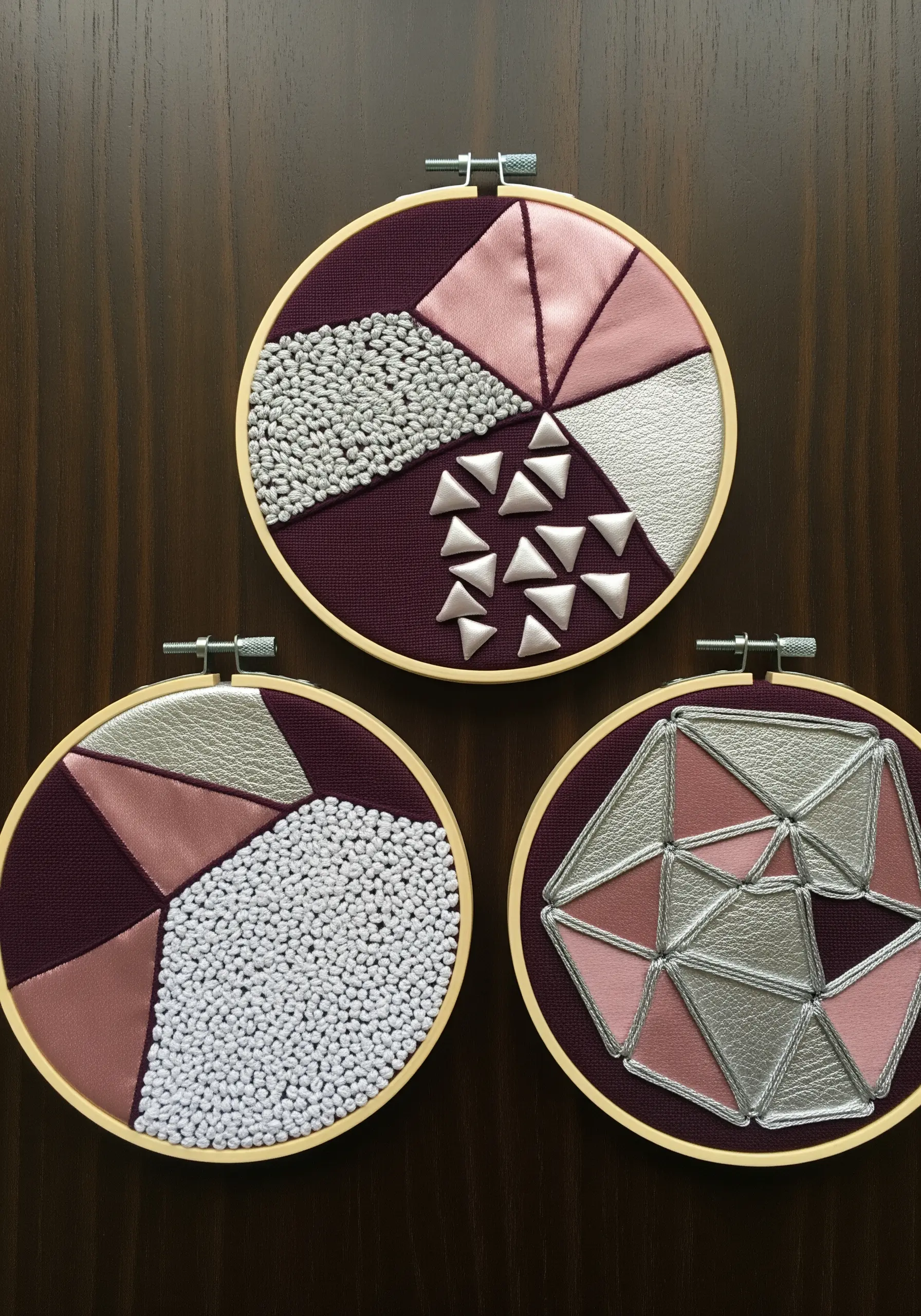 Trio of embroidery hoops with geometric patchwork in pink and silver, featuring beadwork and 3D shapes.