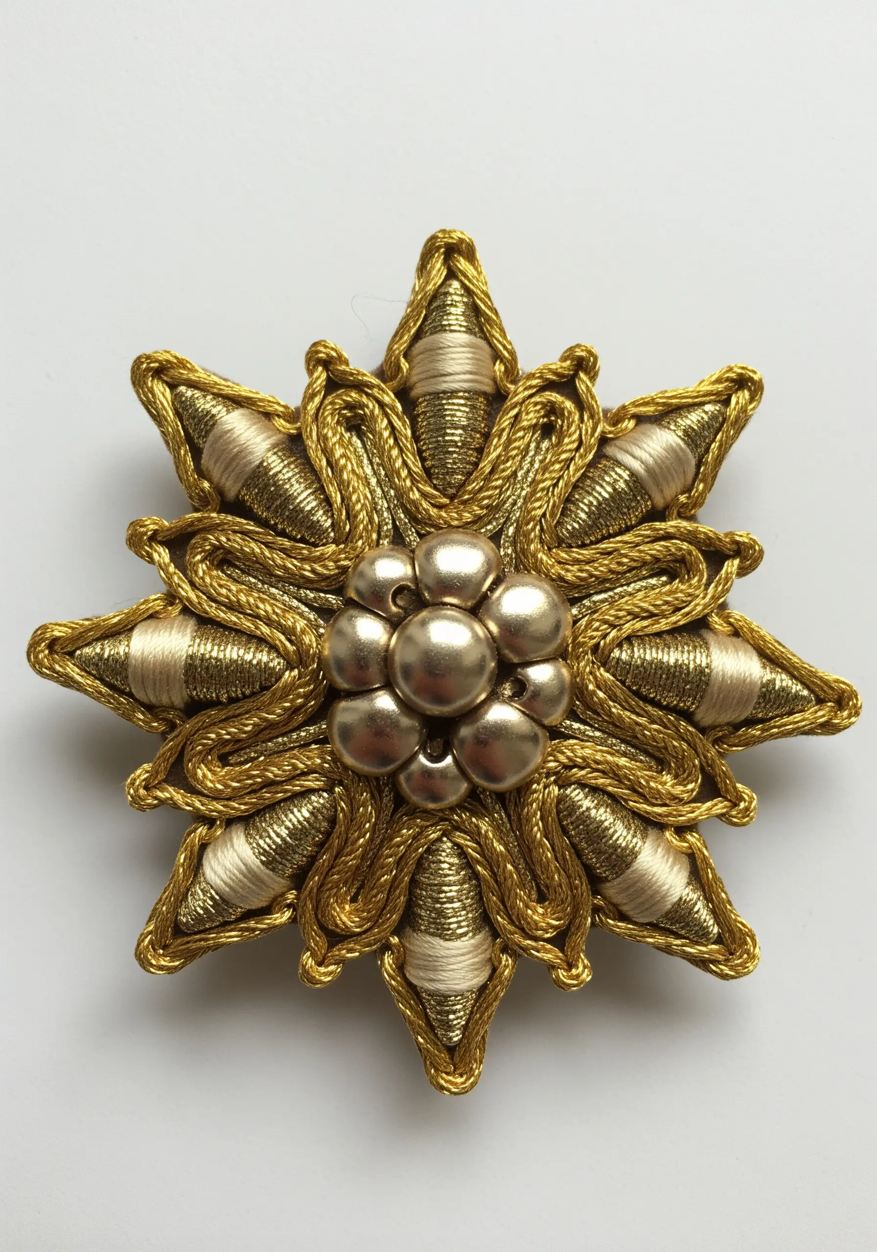 A dimensional goldwork appliqué with wrapped cords and metallic beads in a floral star shape.