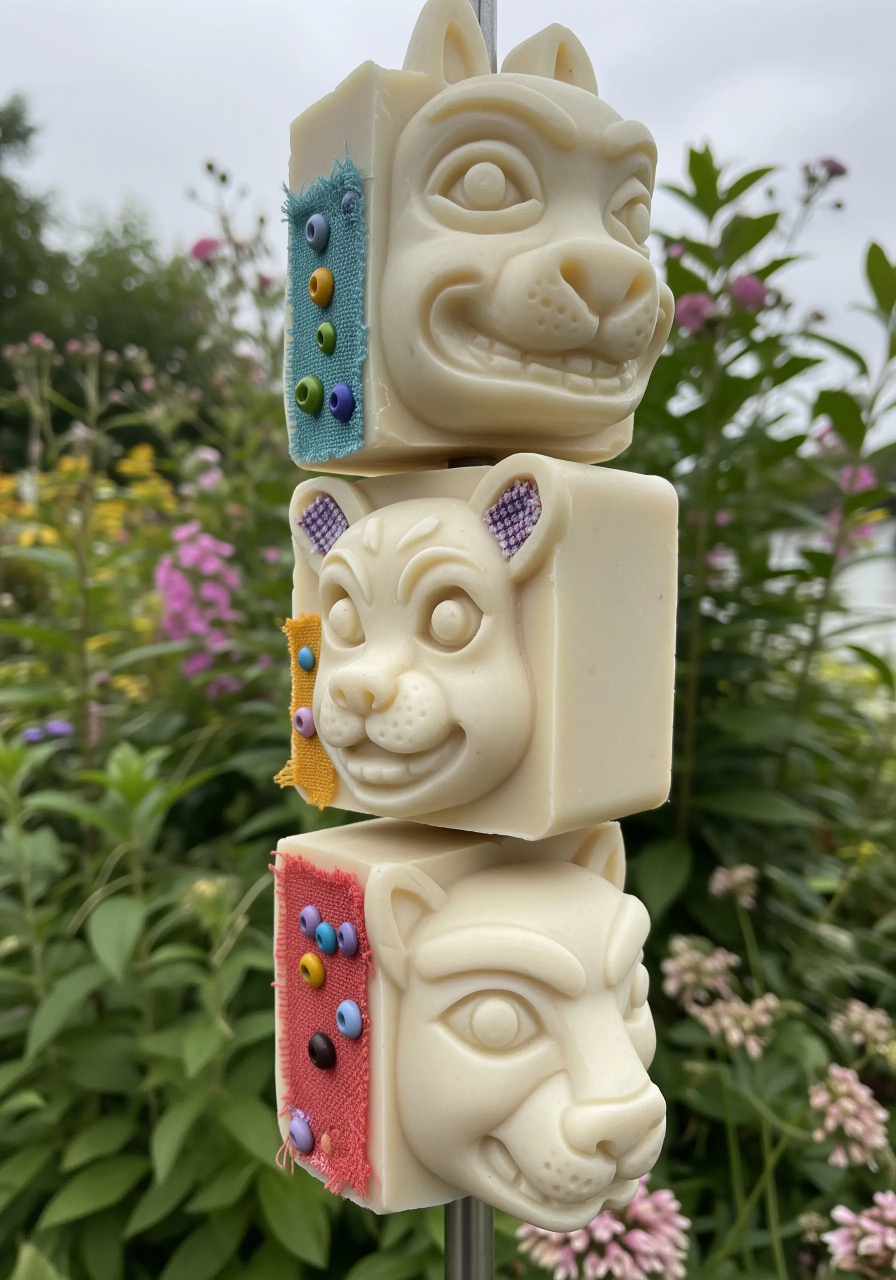 A stack of three carved soap bars, each embellished with a small patch of fabric and beading.