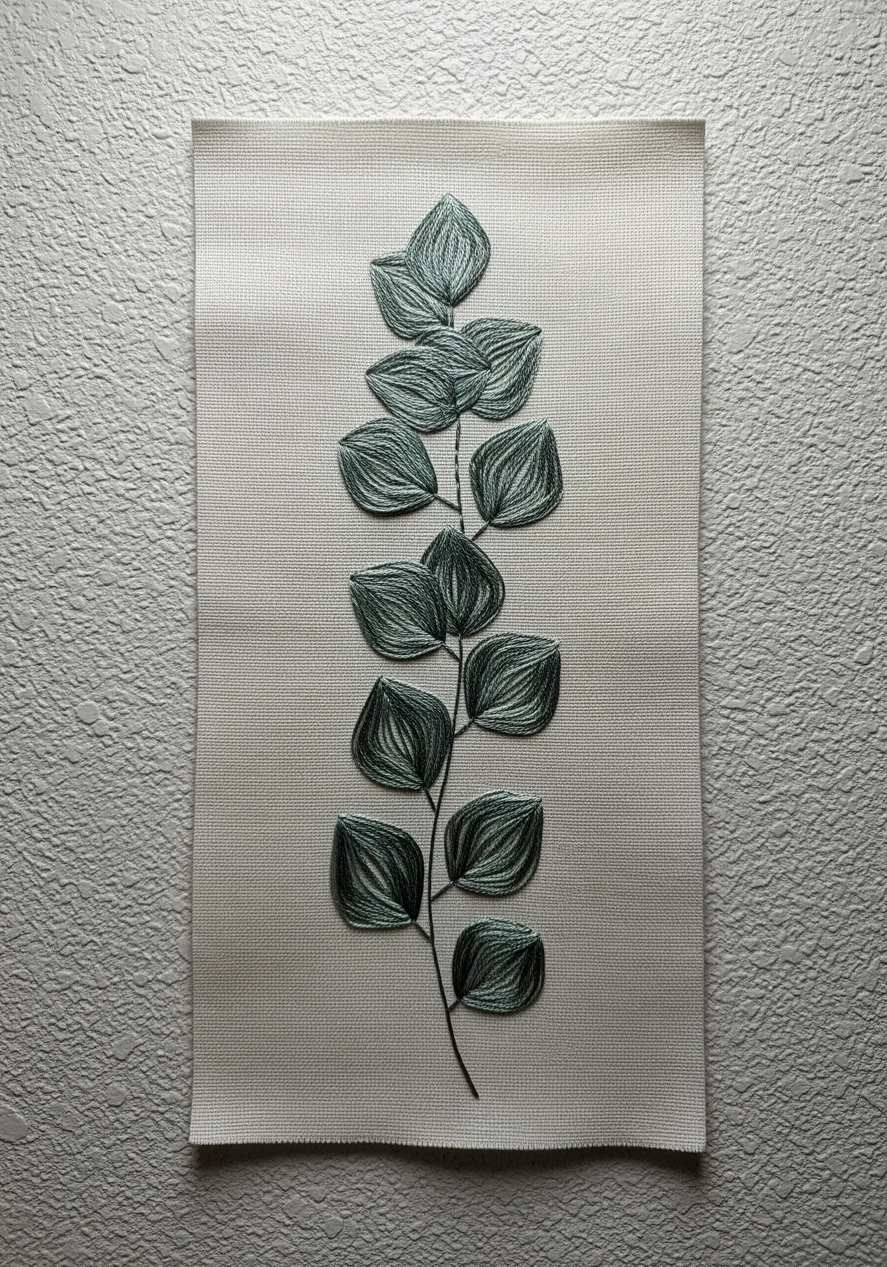 A eucalyptus branch with textured leaves stitched in variegated green thread on light fabric.