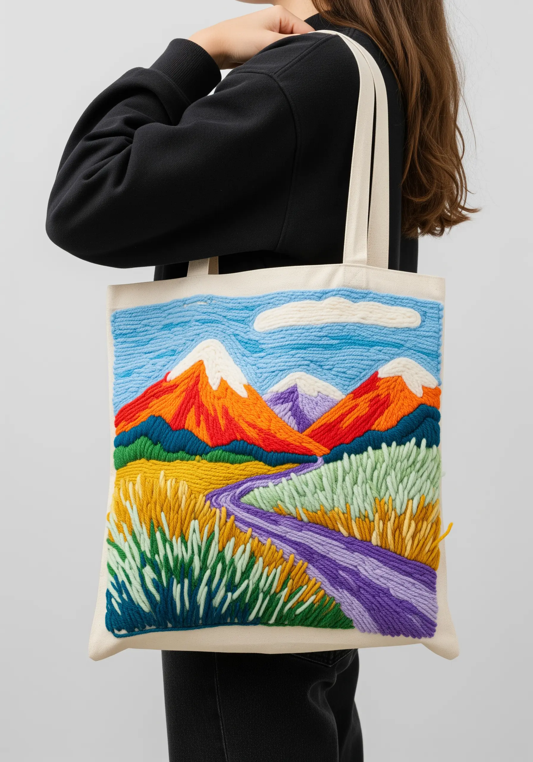 A colorful mountain landscape with a river, created with textural punch needle embroidery on a tote.