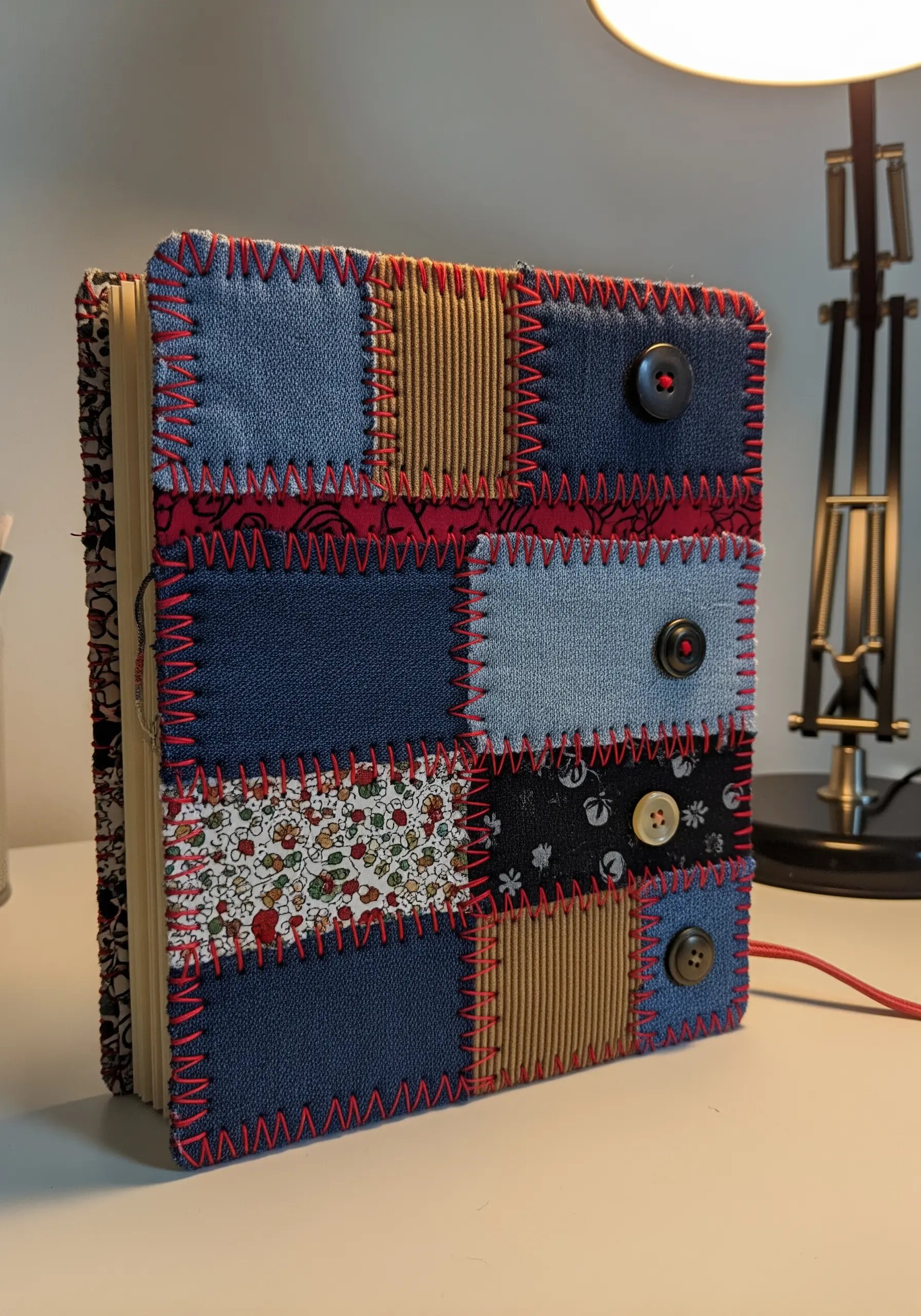 A journal with a patchwork cover made of denim and fabric, stitched with red thread.