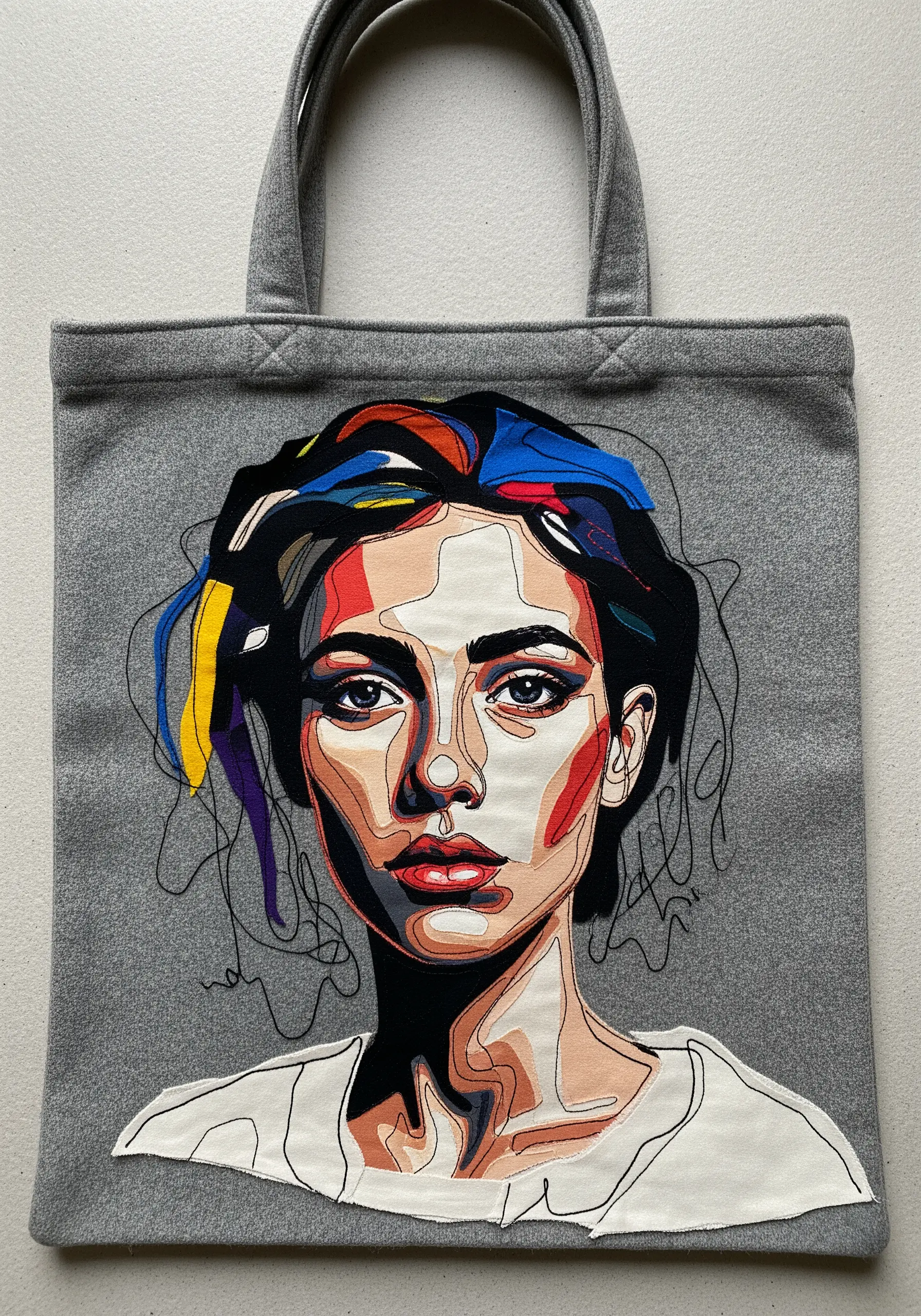 Expressive embroidered and appliquéd portrait on a gray tote with scribbled thread details.