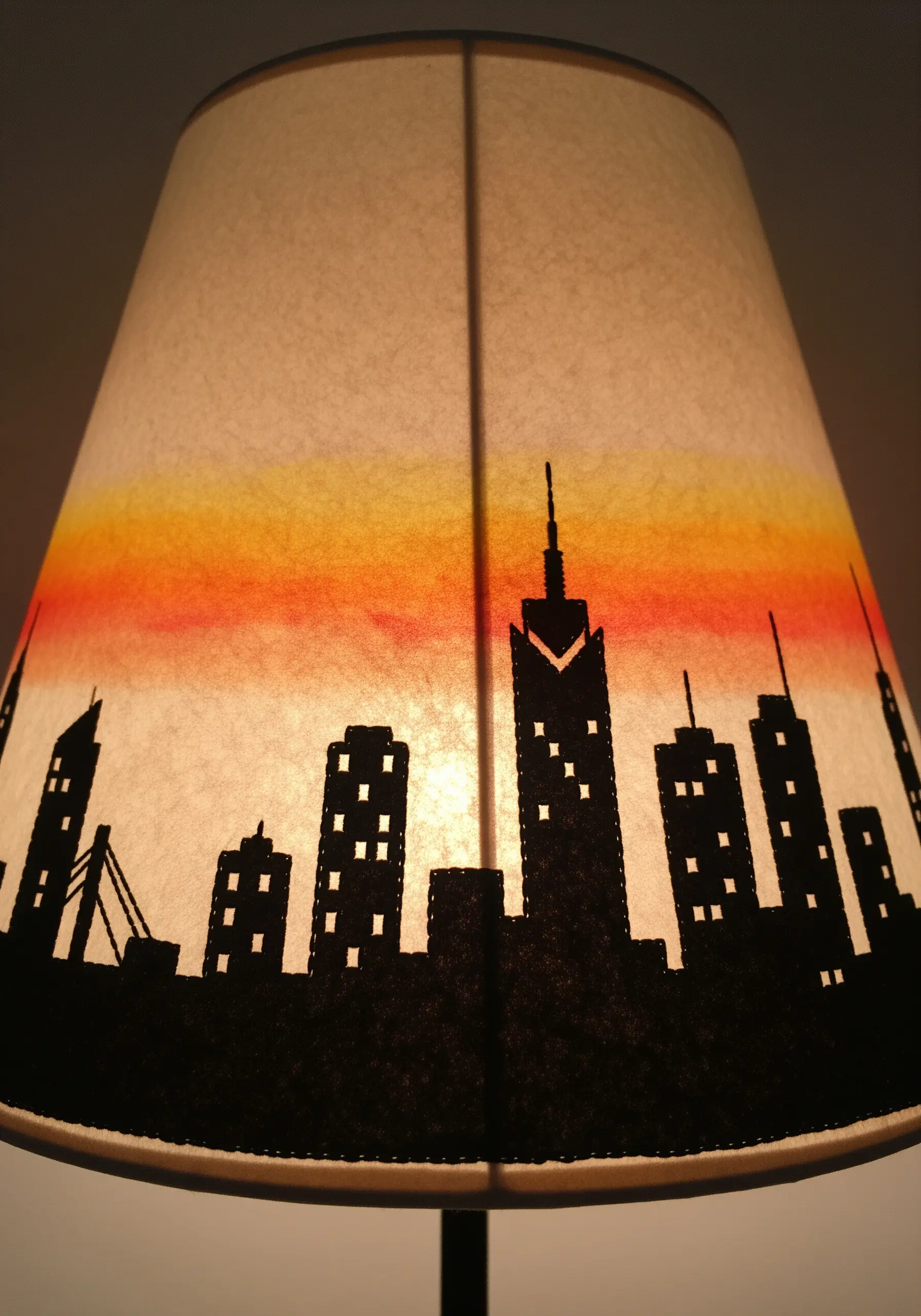 A lampshade with a painted sunset gradient and a black felt city skyline silhouette.