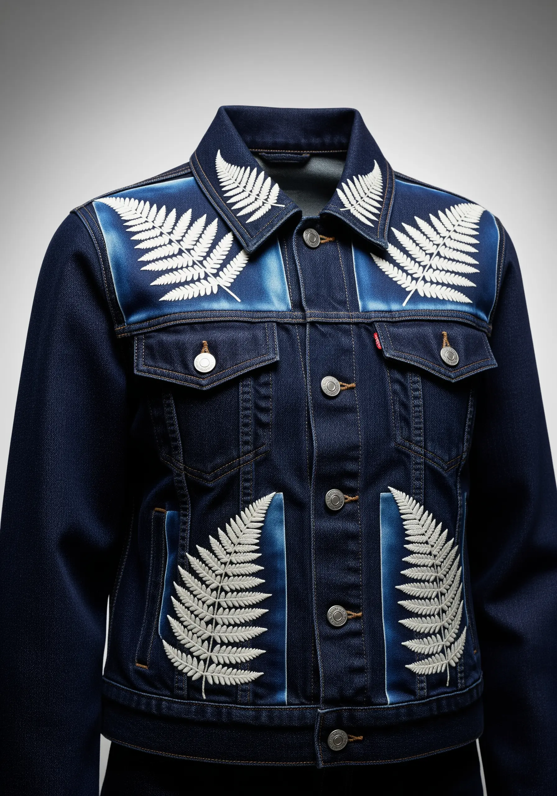 White embroidered ferns on bleached panels of a dark wash denim jacket.