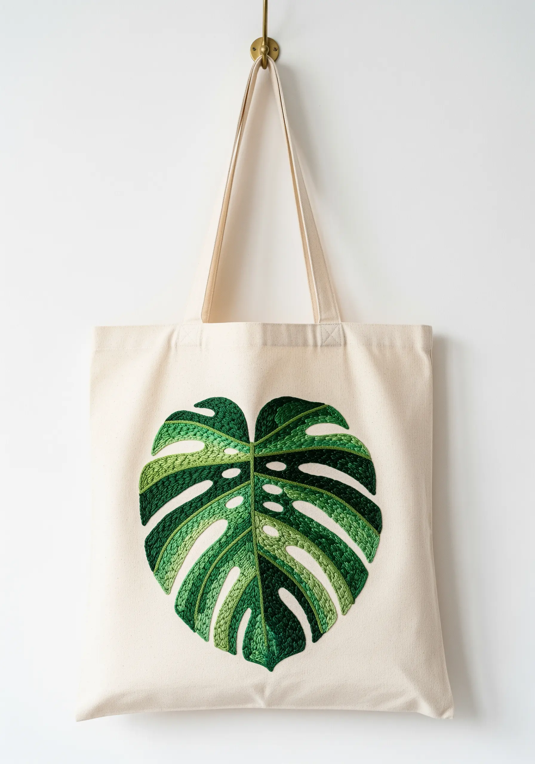 A large monstera leaf embroidered on a canvas tote bag, with segments filled in different green shades.