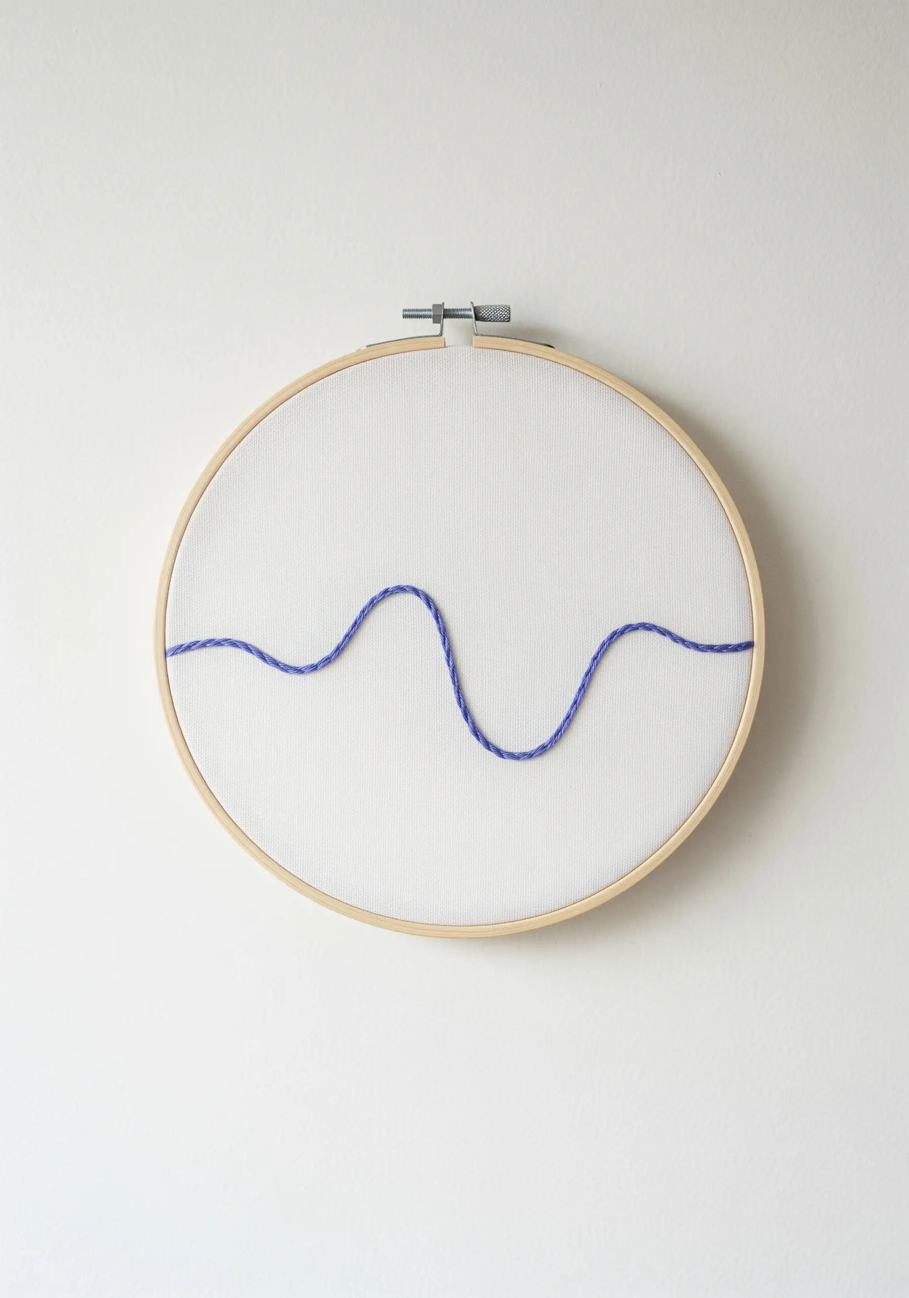 A single, wavy line of purple thread stitched across the center of a simple embroidery hoop.