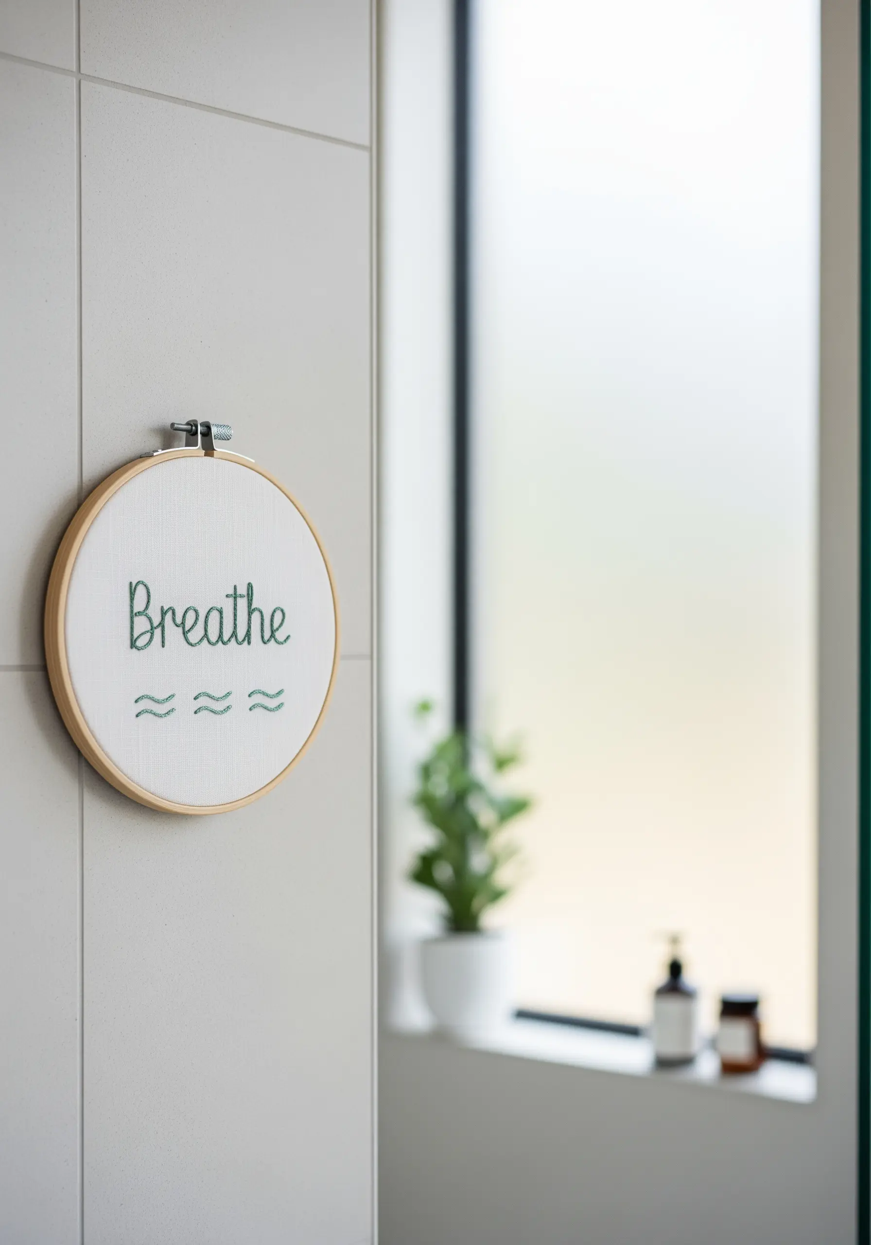 The single word 'Breathe' stitched in a simple script on white fabric in a minimalist bathroom.