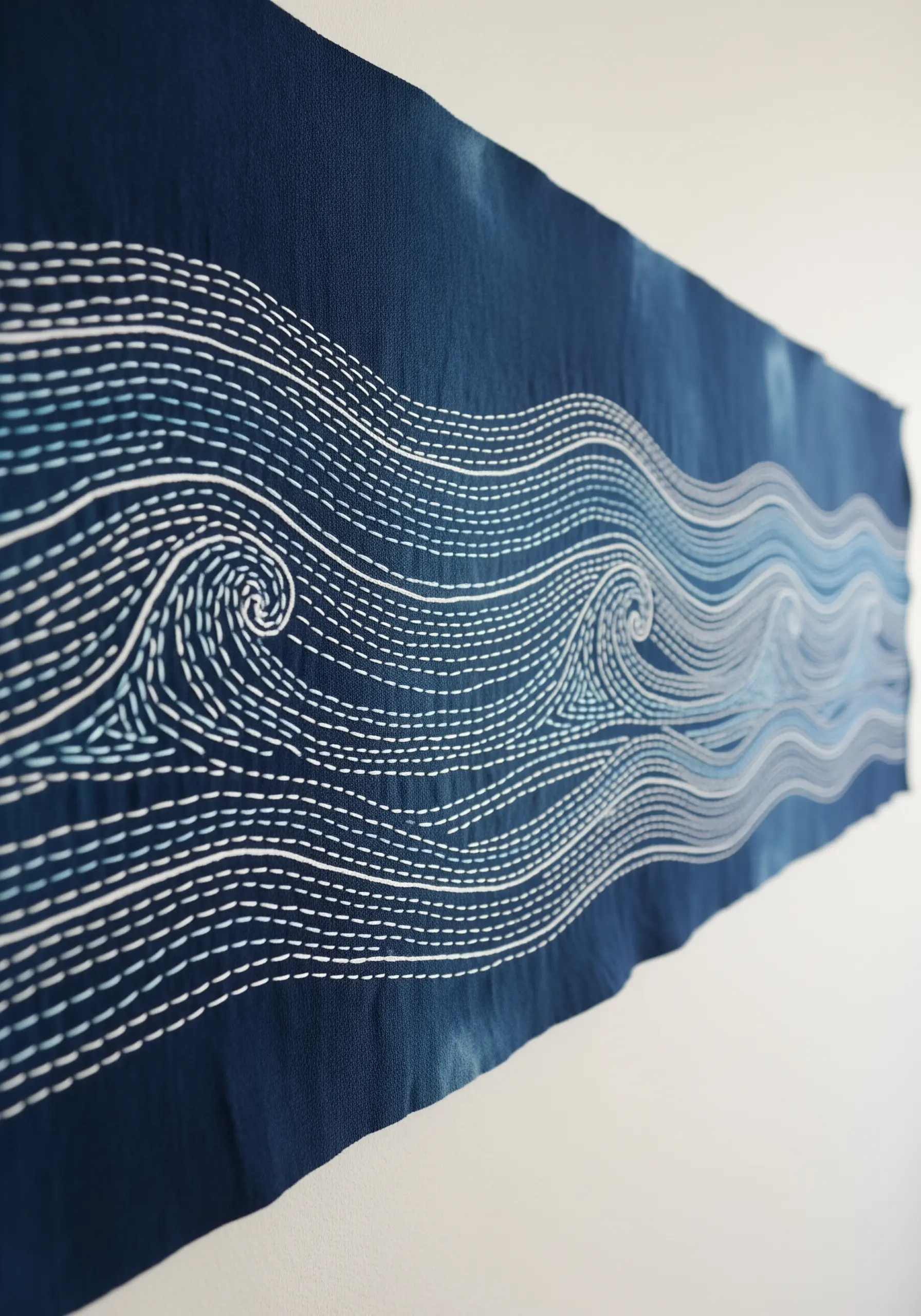 Sashiko-style embroidery of ocean waves in white thread on a dark indigo fabric panel.