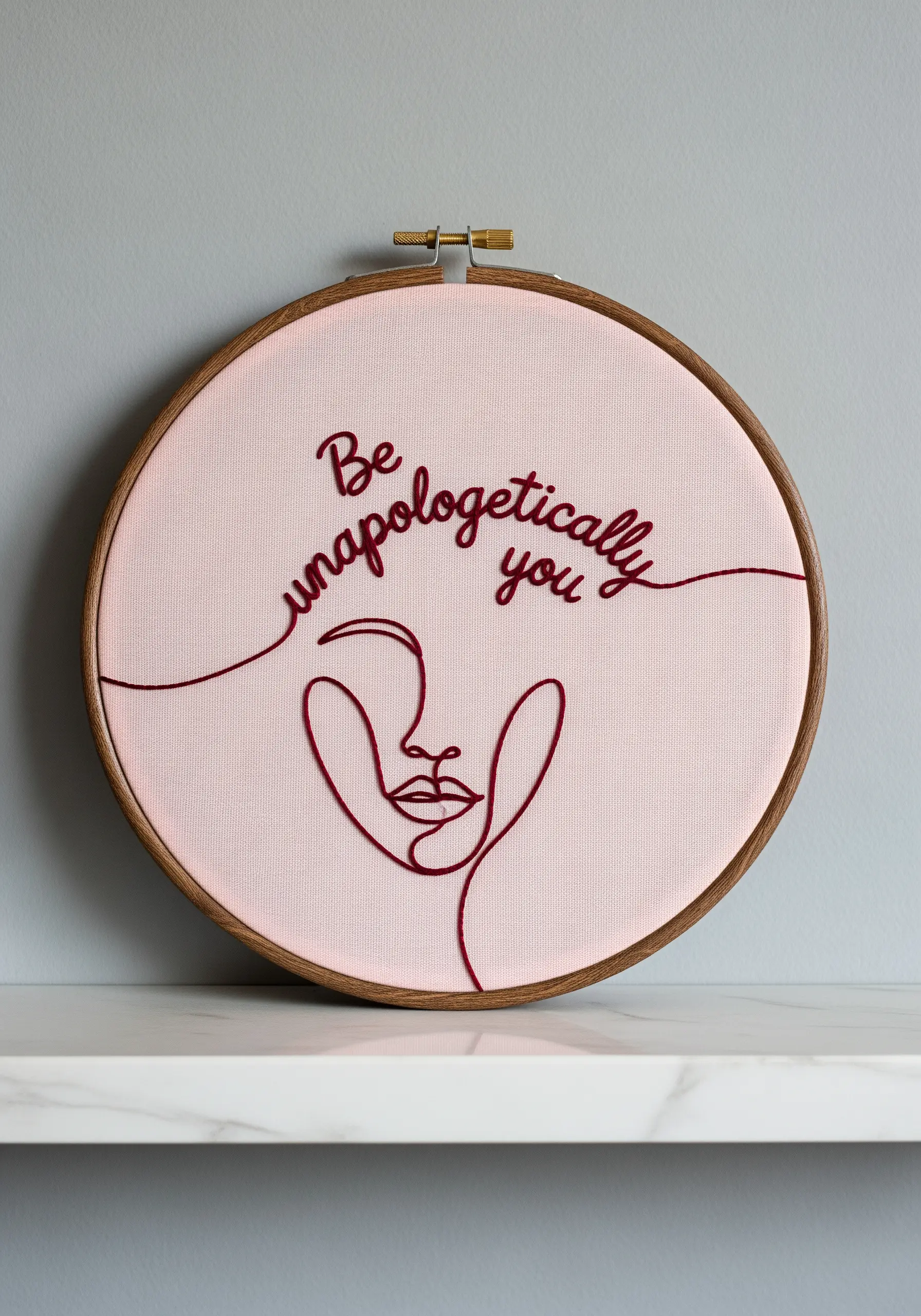 Continuous line art embroidery of a face and quote on pale pink fabric.
