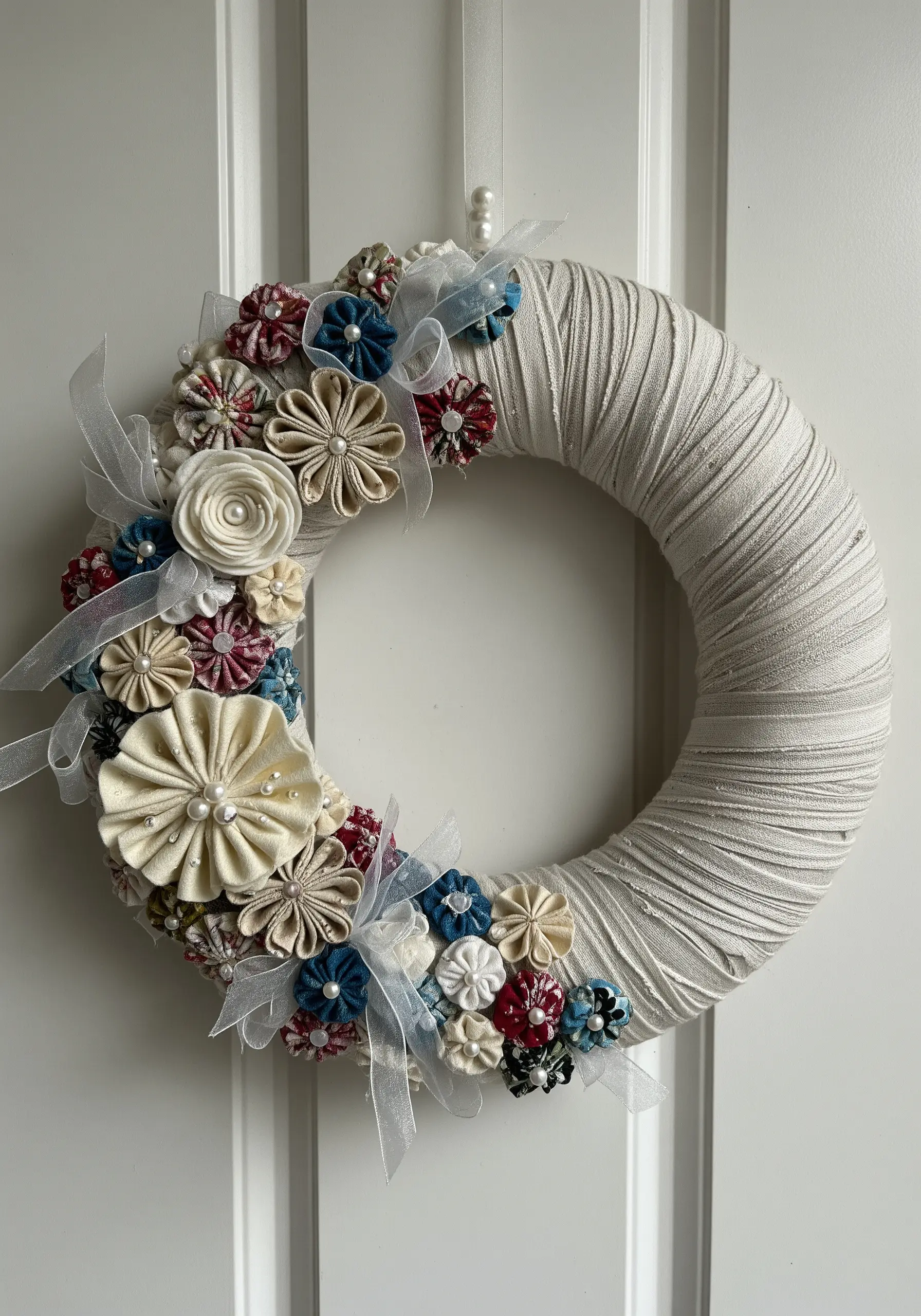 A wreath decorated with handmade fabric flowers in cream, red, and blue.