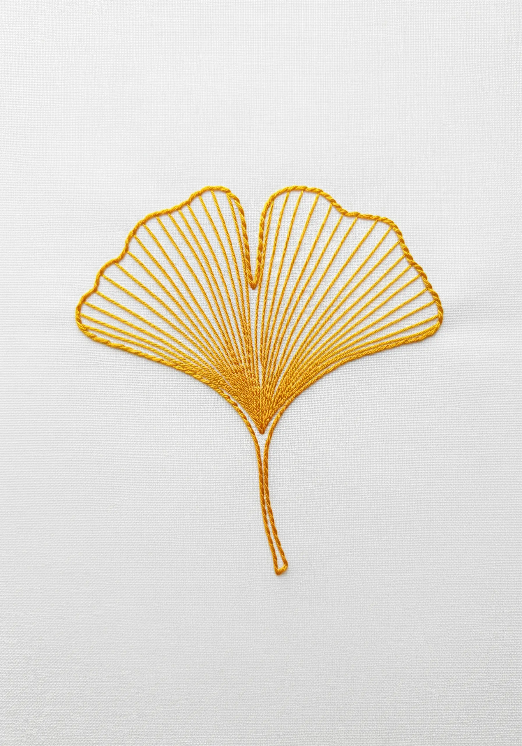A ginkgo leaf embroidered with radiating straight stitches in golden yellow thread.